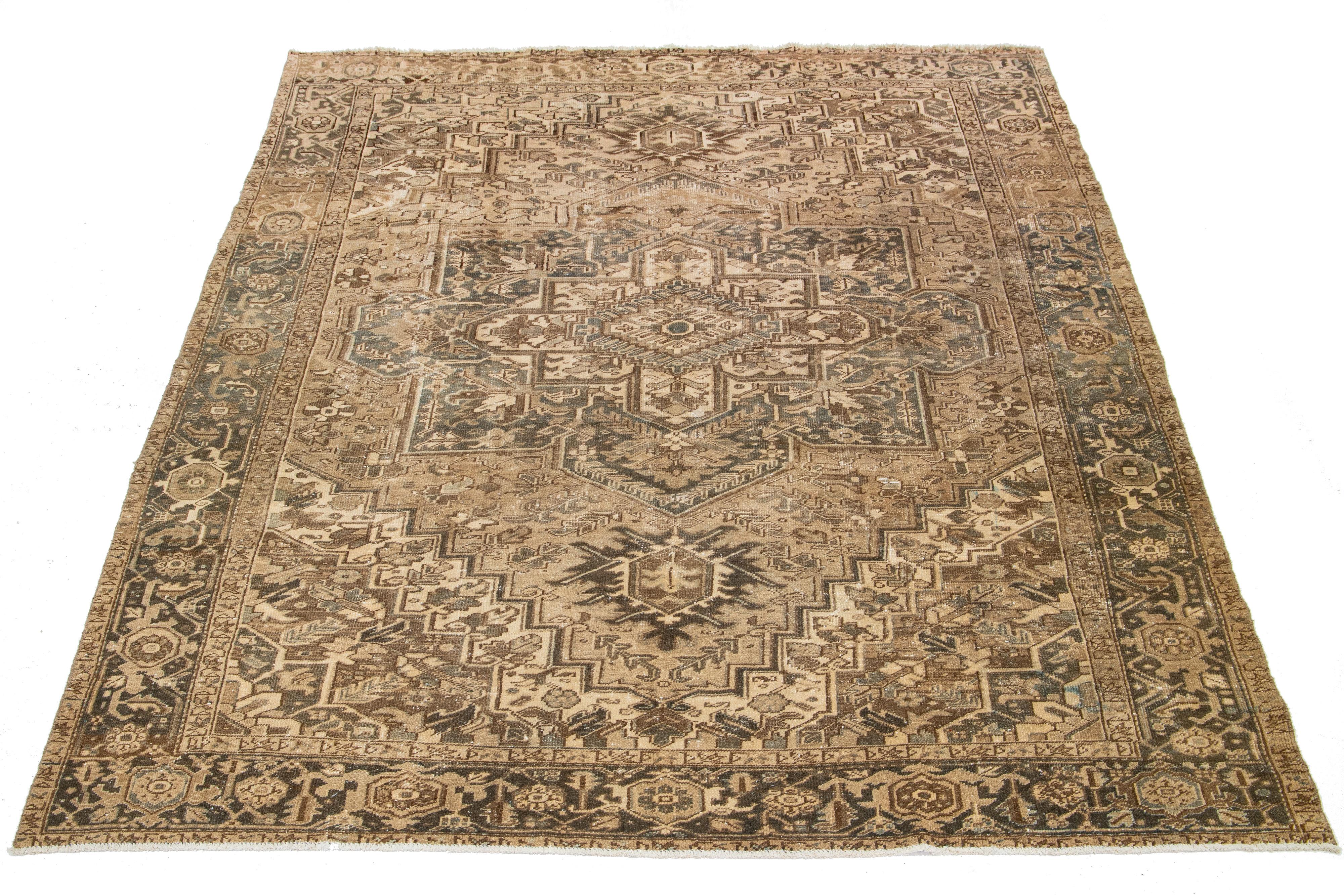 Ce tapis persan Heriz est fabriqué à la main avec de la laine nouée à la main. Le champ du tapis est orné d'un motif captivant de couleur marron, rehaussé de belles nuances de gris et de beige.

Ce tapis mesure 9' x 11'8