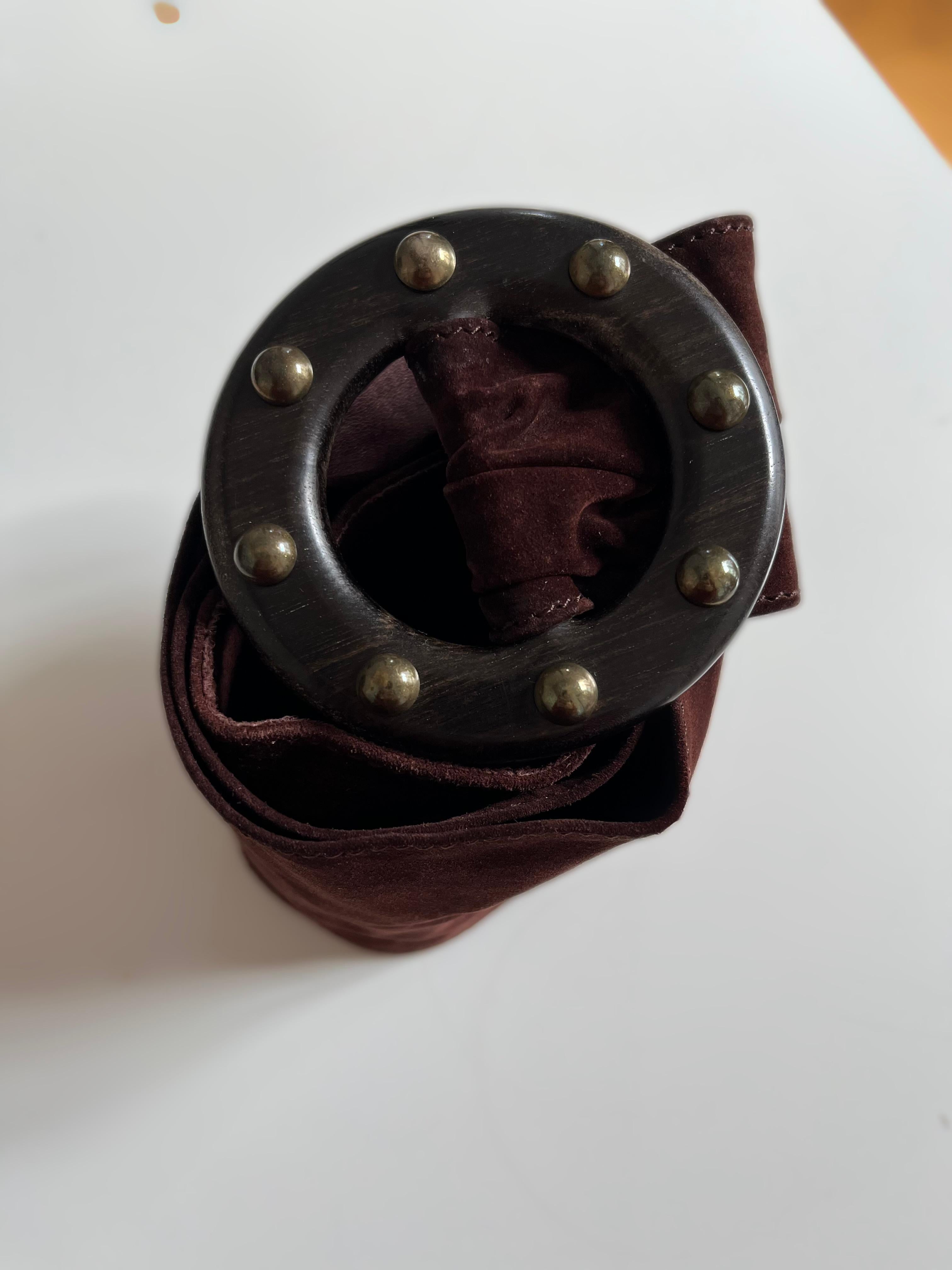 This belt is from the House of SAINT LAURENT. This 80s piece is made of brown suede leather. The buckle is made of ebony with 8 bronze round-shaped studs. On the inside of the belt, we can see the signature 