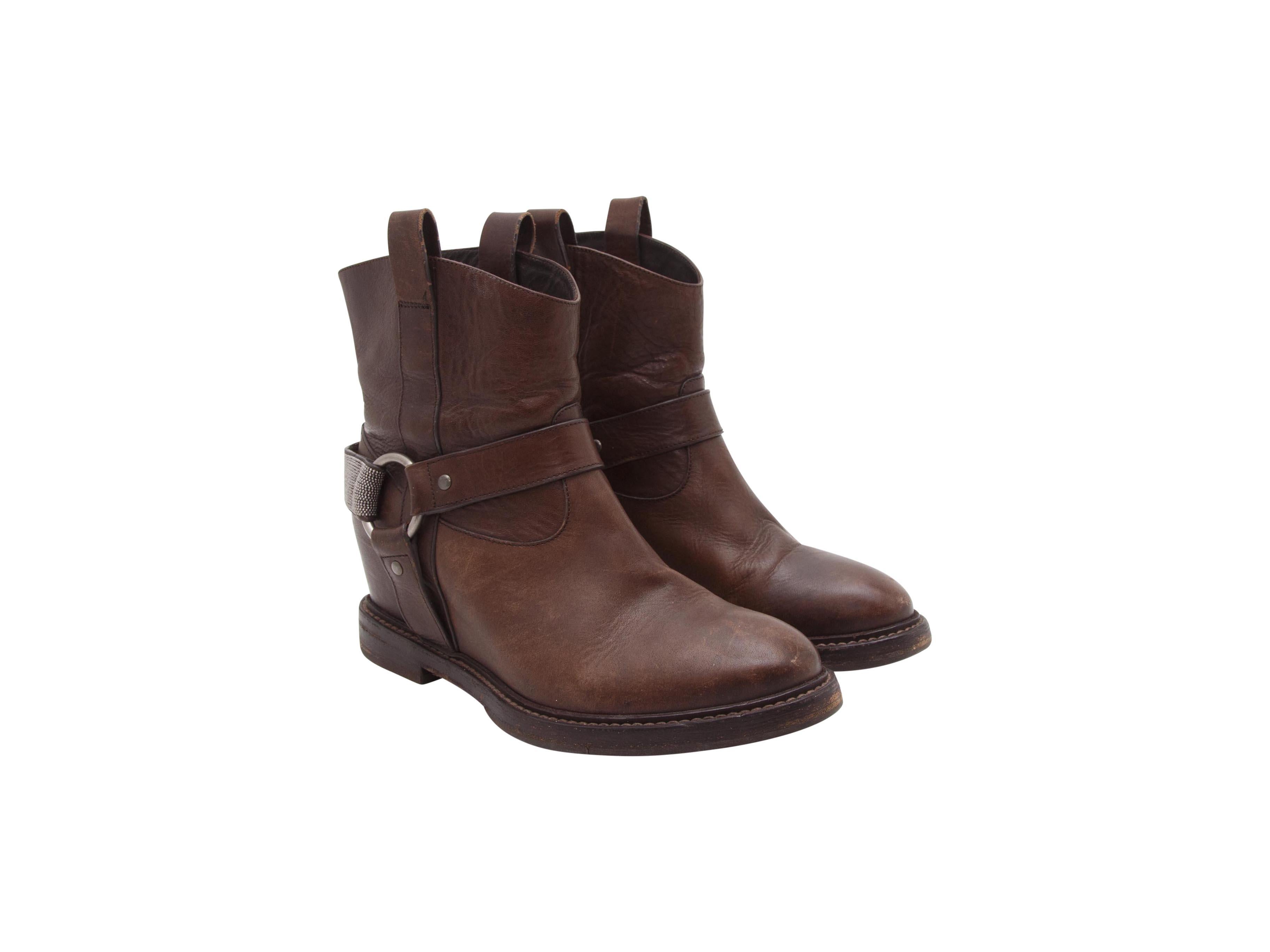 Product details:  Brown leather wedge ankle boots by Brunello Cucinelli.  Embellished Western strap detail.  Round toe.  Hidden wedge heel.  Silvertone hardware.  1