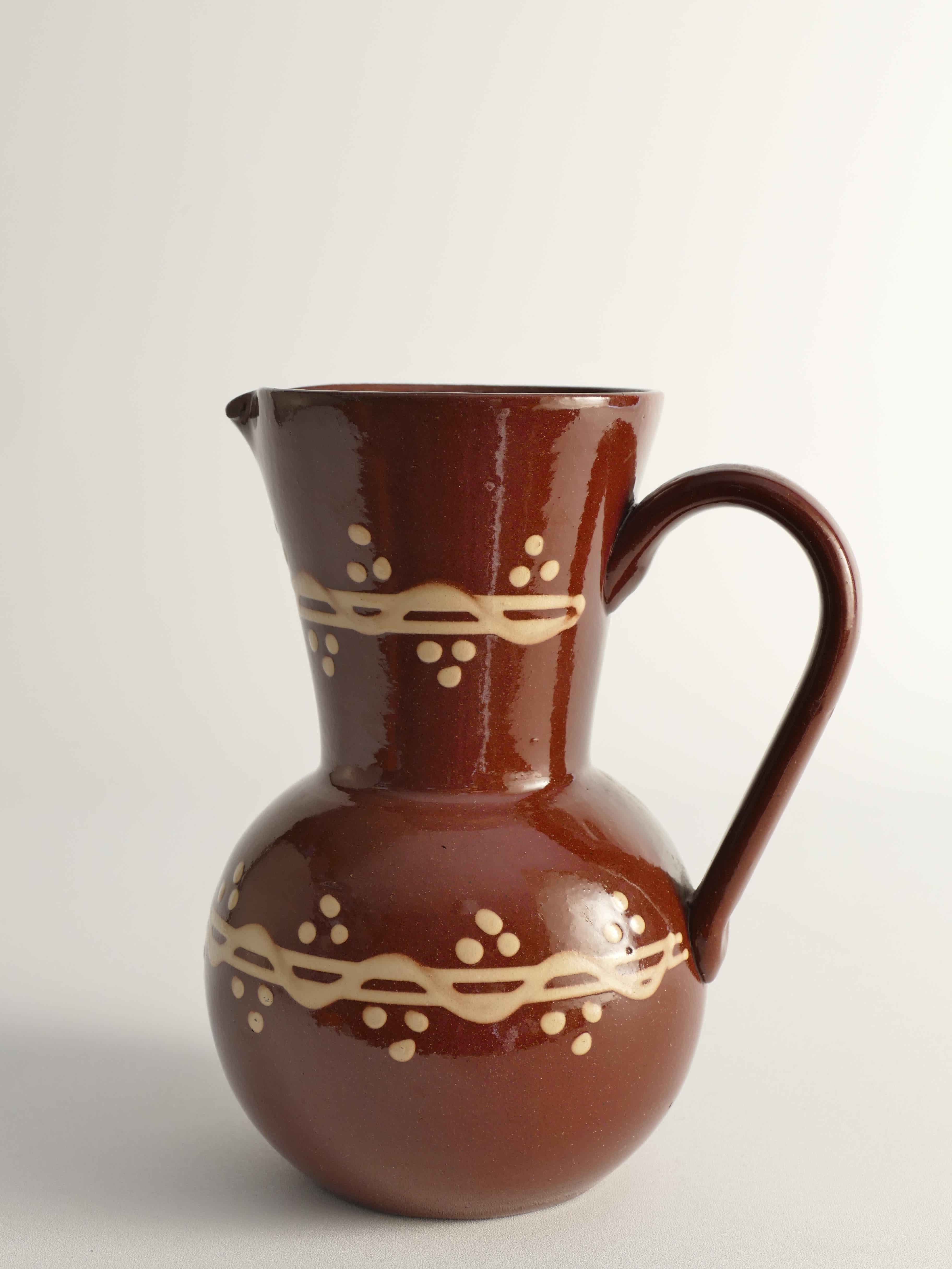 Questa rara brocca o vaso in gres svedese, realizzata da Andersson & Johansson per Höganäs in Svezia, presenta un corpo marrone con decorazioni bianco crema. Progettata da John Andersson negli anni '20, presenta una forma fortemente modernista che