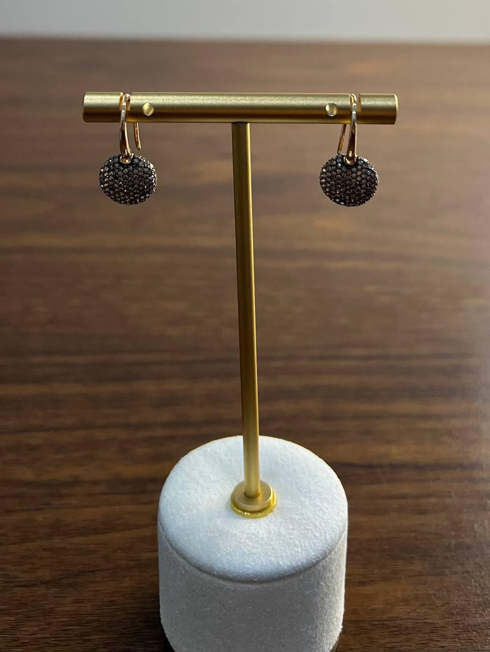 A pair of elegant earrings with a modern design.
Crafted with precision, these earrings feature round, textured discs encrusted with brown, champagne shimmering diamonds.
The discs are suspended from sleek, gold-toned hooks, adding a touch of