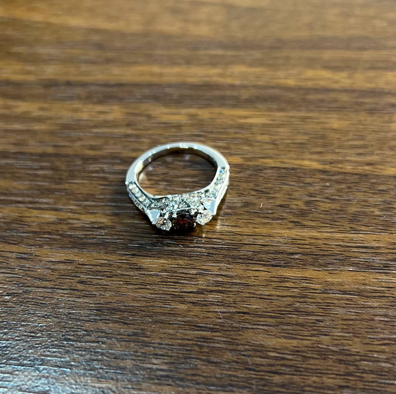 Discover the allure of this exquisite ring, a testament to refined craftsmanship.

Crafted in lustrous metal, this piece features a central brown diamond flanked by two smaller stones, creating a harmonious trio. The band is adorned with a series of