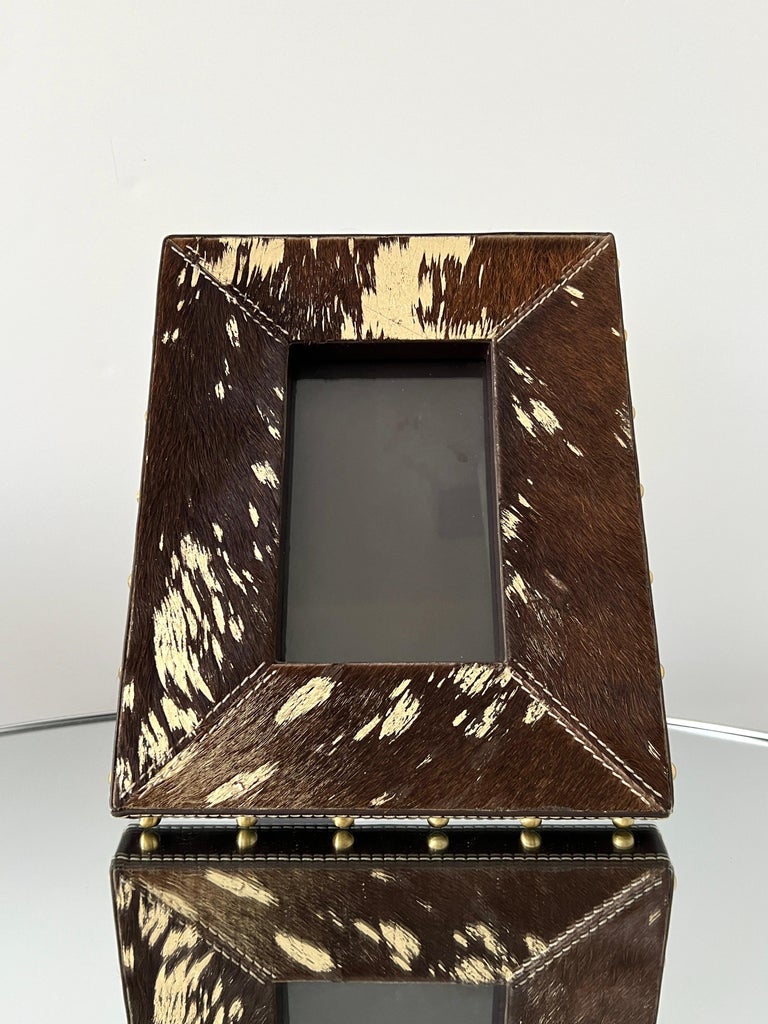 Rustic picture frame in dark brown cowhide with gold metallic foil accents. Handcrafted and features brown leather borders with brass studs and handstitched details. Frame is 8.5