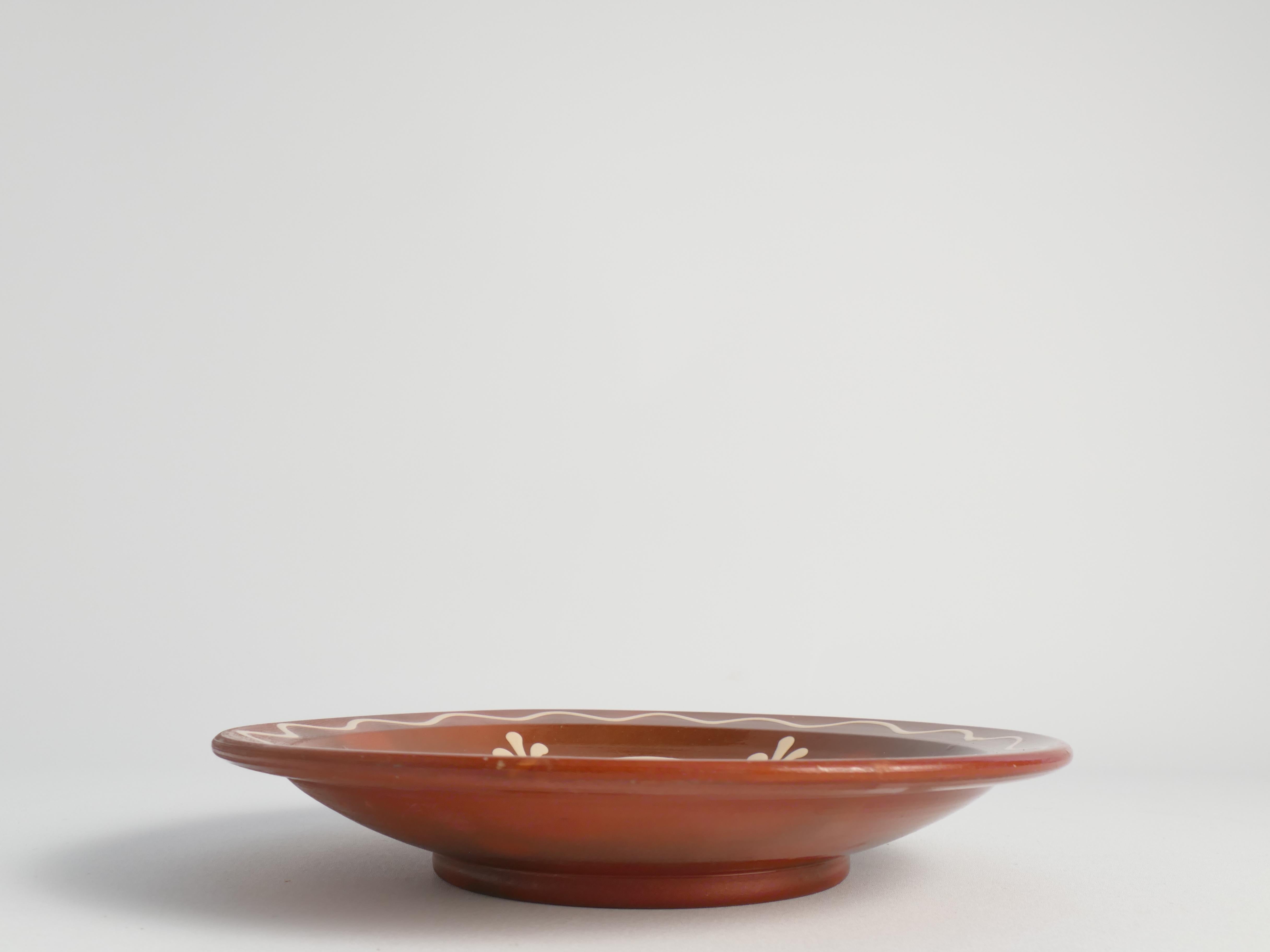 Questo squisito piatto decorativo scandinavo in gres o Boel di Andersson & Johansson, Höganäs, è caratterizzato da motivi tradizionali di arte popolare in bianco su un ricco sfondo marrone terracotta. 

Ispirato alla tradizione pittorica dell'arte