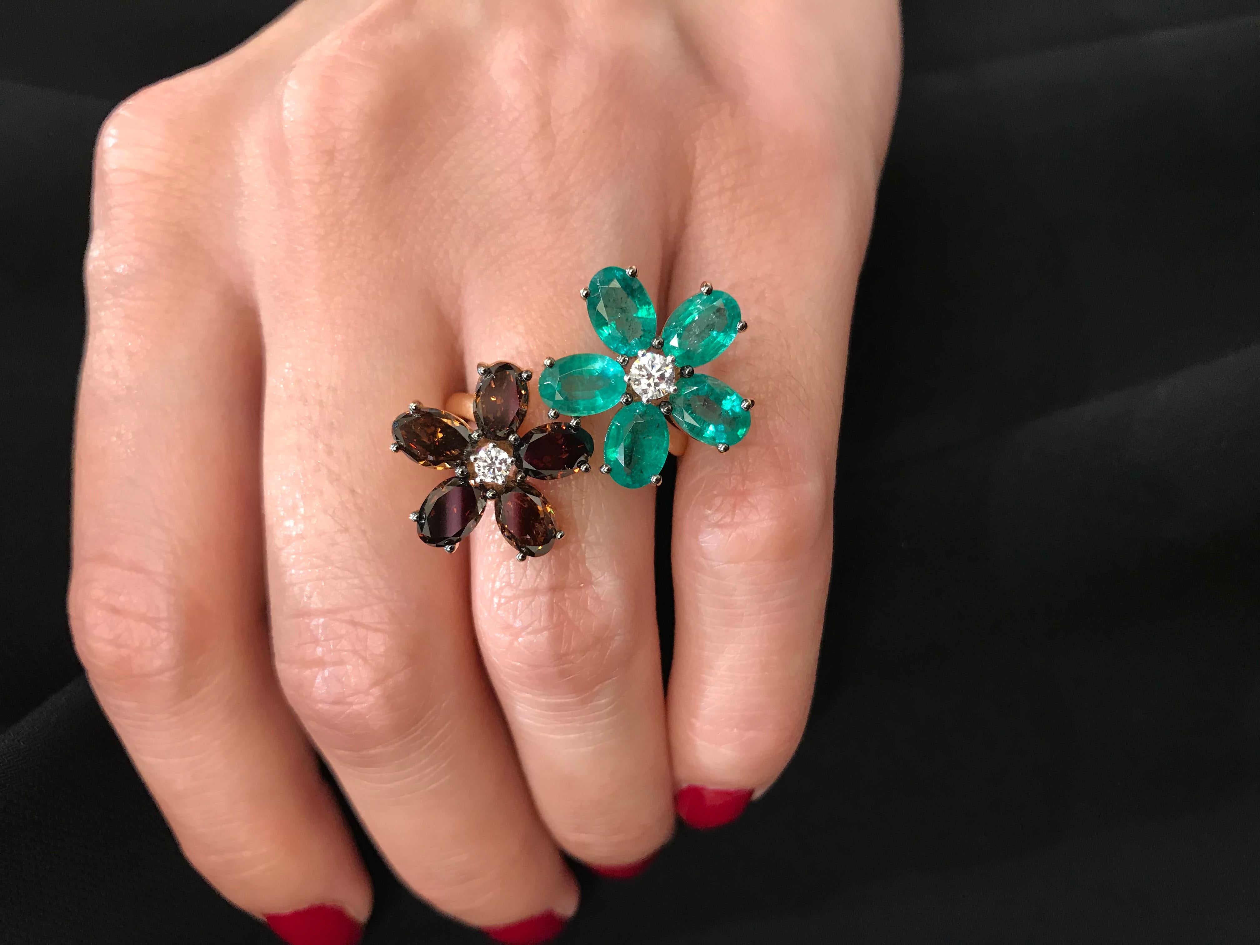 Brown diamonds and emeralds are in a harmonious match in this 18K rose gold double ring. 
The flowers are slightly asymmetrical. 
One flower is made up of five brown diamond 