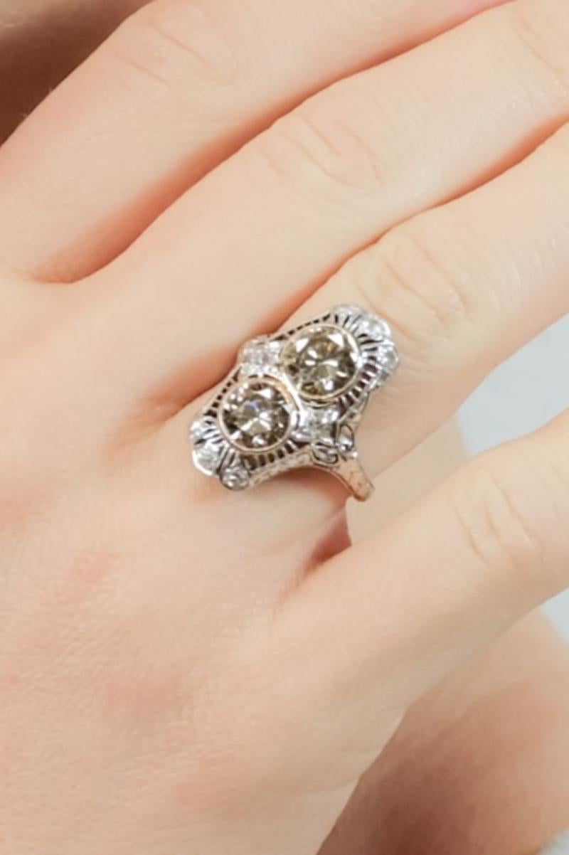 Questo anello presenta due diamanti marroni, del peso di circa 3,5 carati, di colori diversi, uno più giallo medio e uno più arancione. Le pietre sono circondate da diamanti più piccoli, del peso di circa 0,40 carati. 