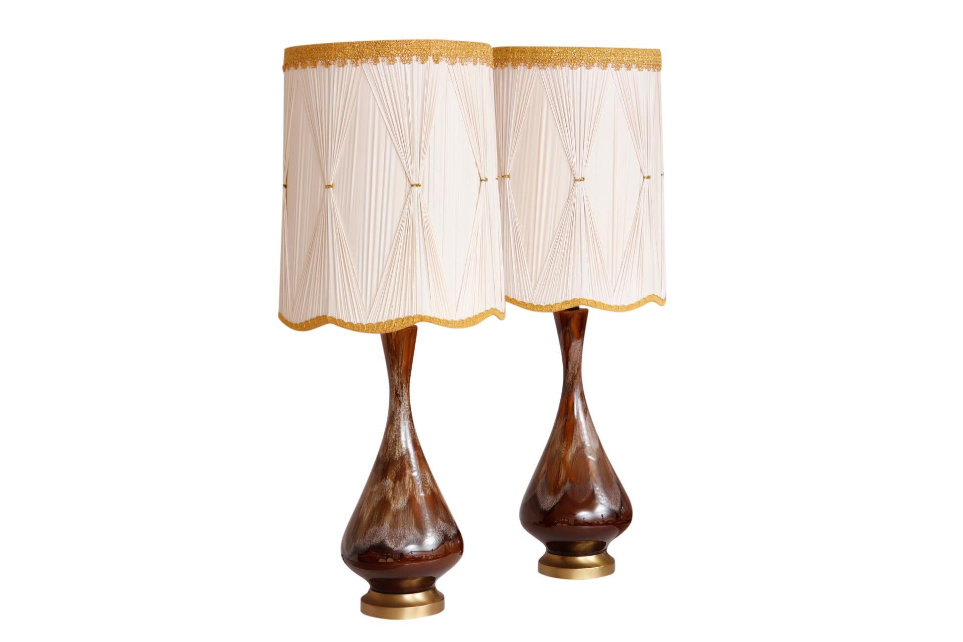 A pair of mid century drip glaze ceramic table lamps with custom shades. Round vases with slender necks are decorated in earthy shades of brown. Round beveled bases are made of brass. Shades are custom made of vinyl with pinched pleats trimmed with