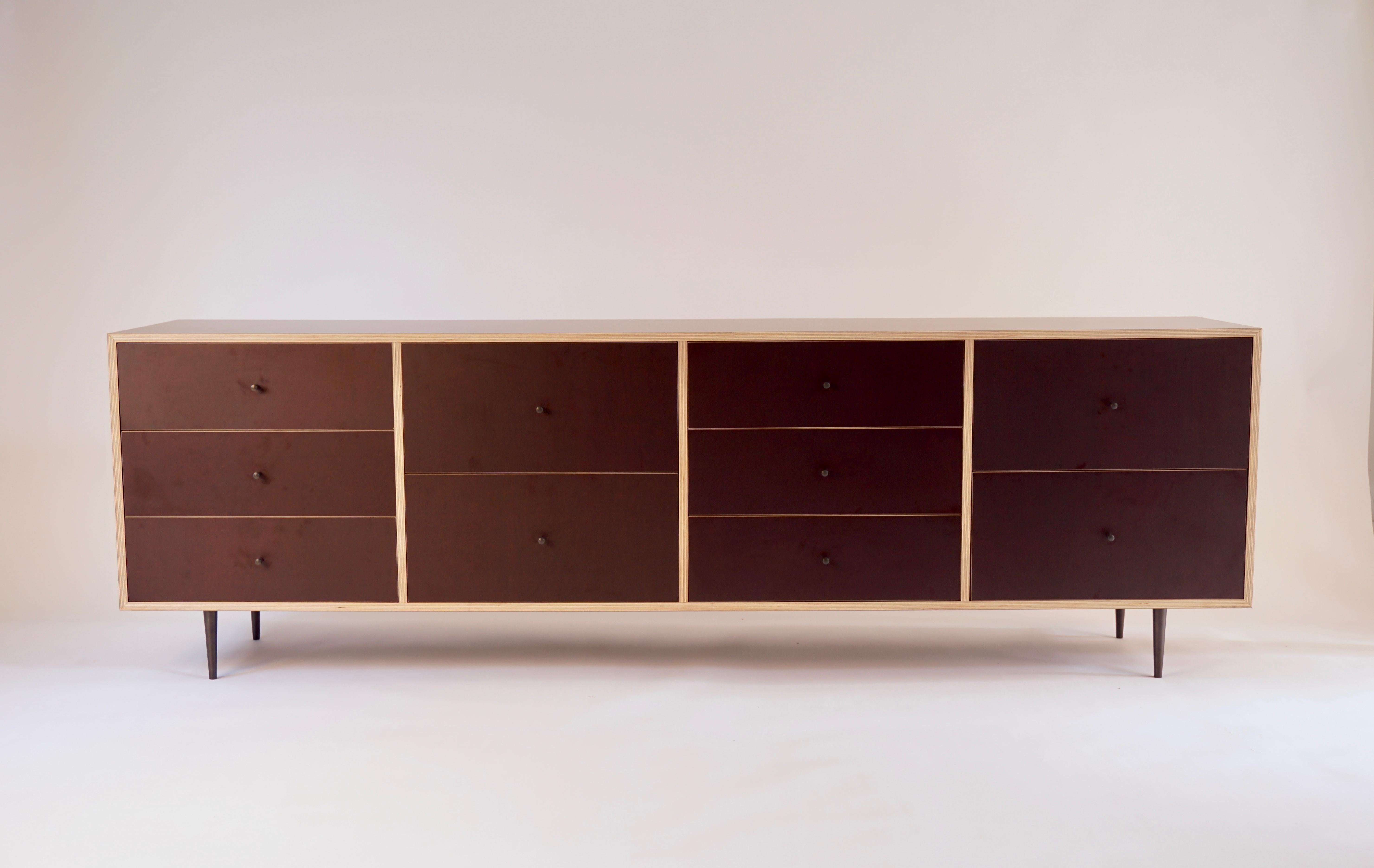 Cette version de l'armoire Classic Finn Ply a été réalisée dans la teinte classique du brun chocolat. Ce meuble comporte quatre rangées de tiroirs, soit dix au total.  Les boutons et les pieds en bronze sont tournés/fabriqués dans notre Studio et