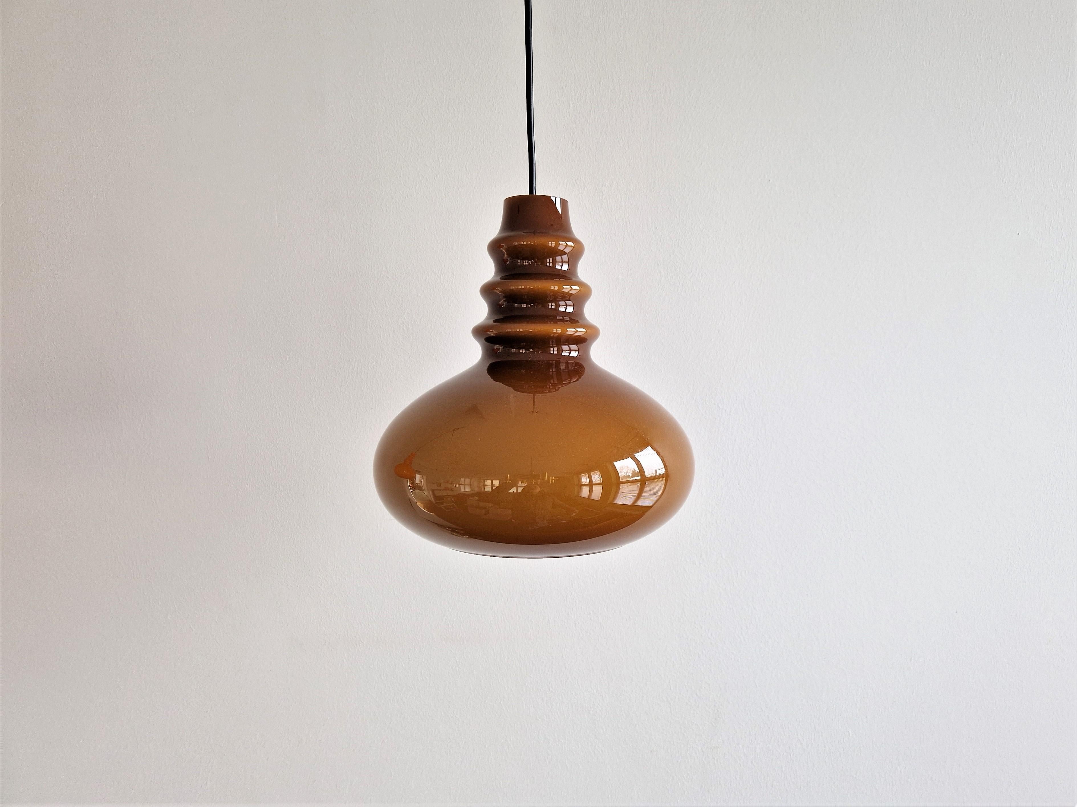This pendant lamp in a beautiful retro shape and form was made by the German manufacturer Peill & Putzler. It is made of double-layerd hand blown Murano glass with an brown outside and an opal white inside. When lit it creates a warm and atmospheric