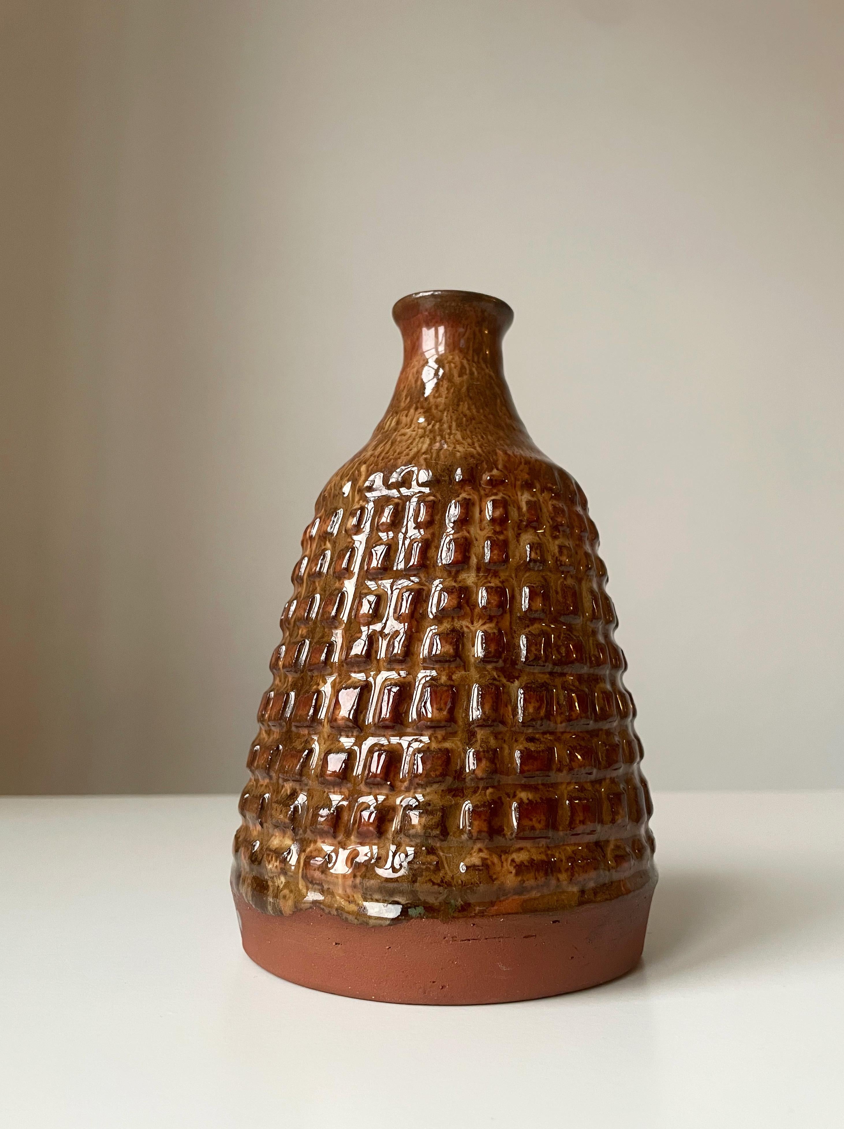 Heavy Danish midcentury modern handmade cone shaped stoneware vase with umber, caramel and hickory brown colored running glaze over square shaped relief stud decorations in an organic pattern around the belly. Slim neck and raw terracotta red clay