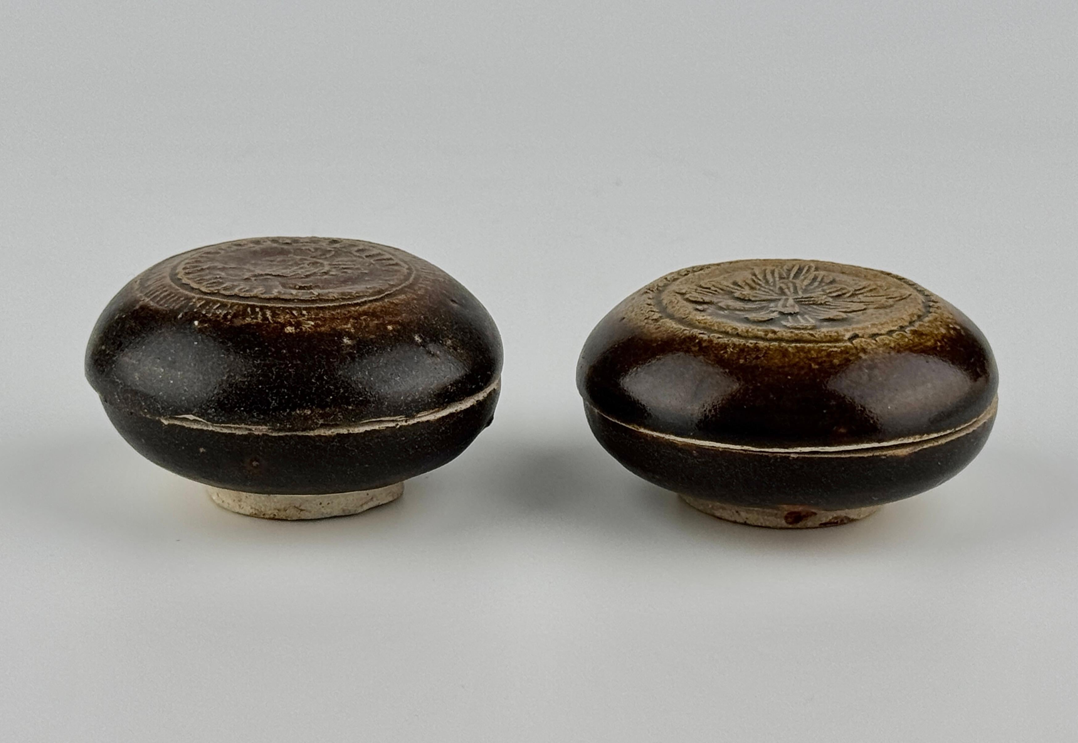 The circular domed cover moulded with a brown glaze that falls short of the straight foot. The pattern on the left features a central circular design with simple shapes and lines carved inside, surrounded by small oval decorations in a ring. On the