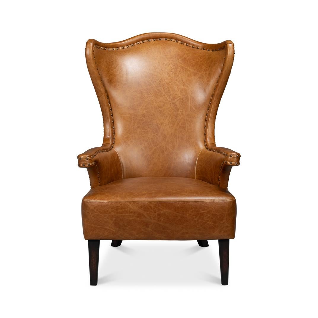 Upholstered in rich, full-grain Cuba brown leather, this chair features a dramatic high-back design that creates an elegant silhouette. The winged sides and gently curved arms are accentuated with meticulous nailhead trim, adding a refined touch of