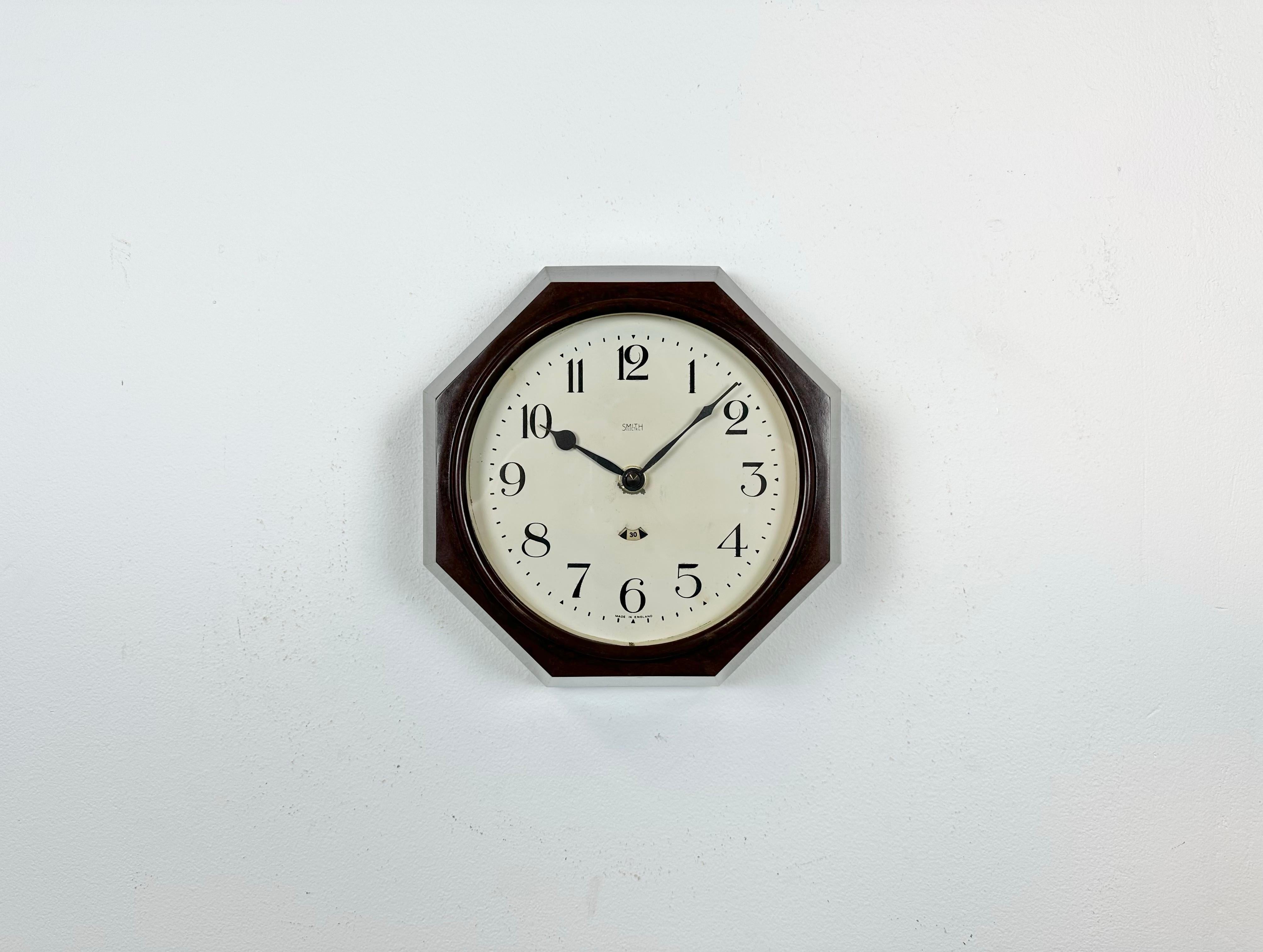 This wall clock was produced by Smith electric in England during the 1950s. It features a brown bakelite frame, an iron dial, an aluminium hands and a clear glass cover. The piece has been converted into a battery-powered clockwork and requires only