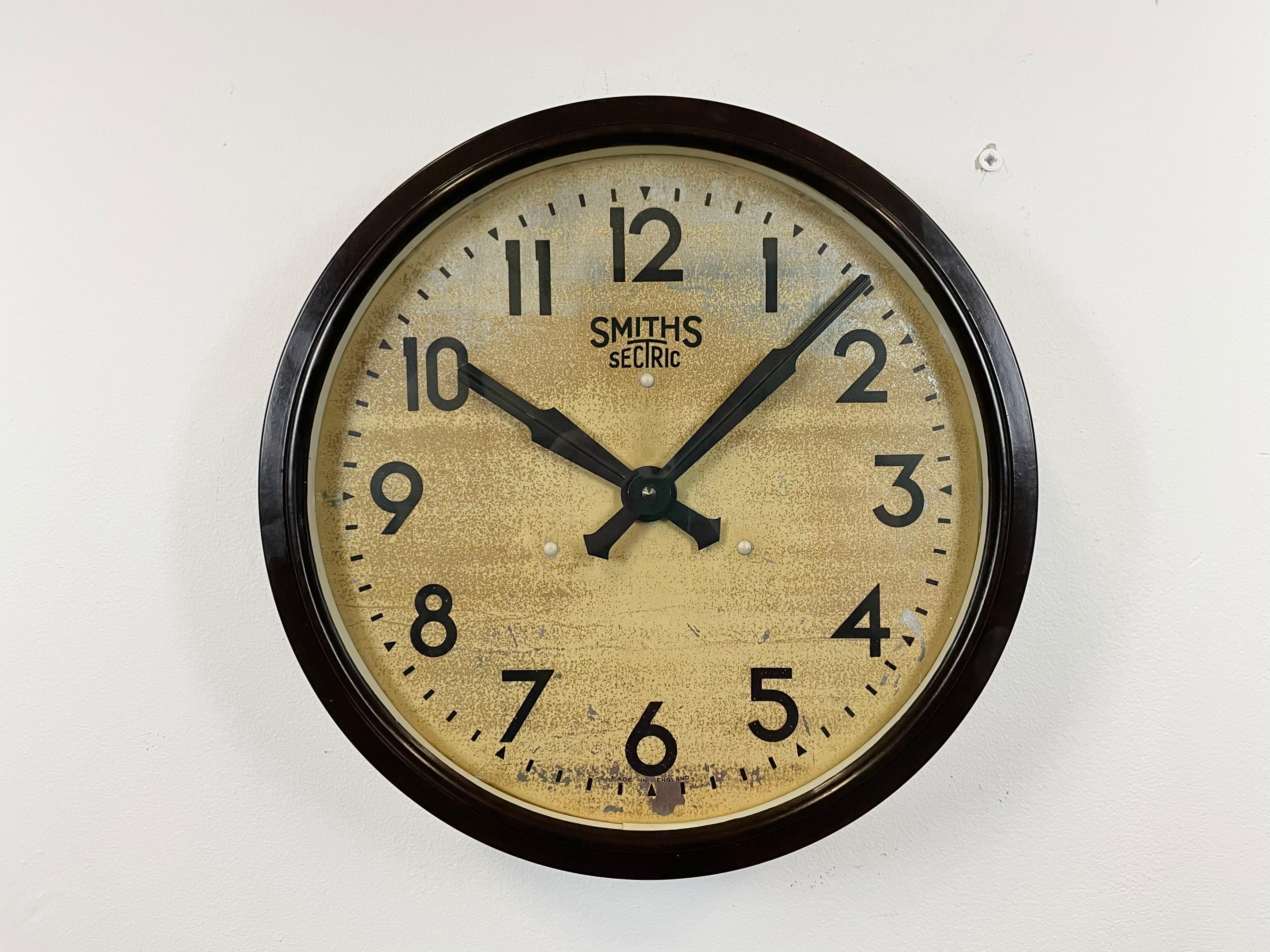 This wall clock was produced by Smith Sectric in England during the 1930s. It features a brown bakelite frame, an iron dial, an aluminium hands and a clear glass cover. The piece has been converted into a battery-powered clockwork and requires only