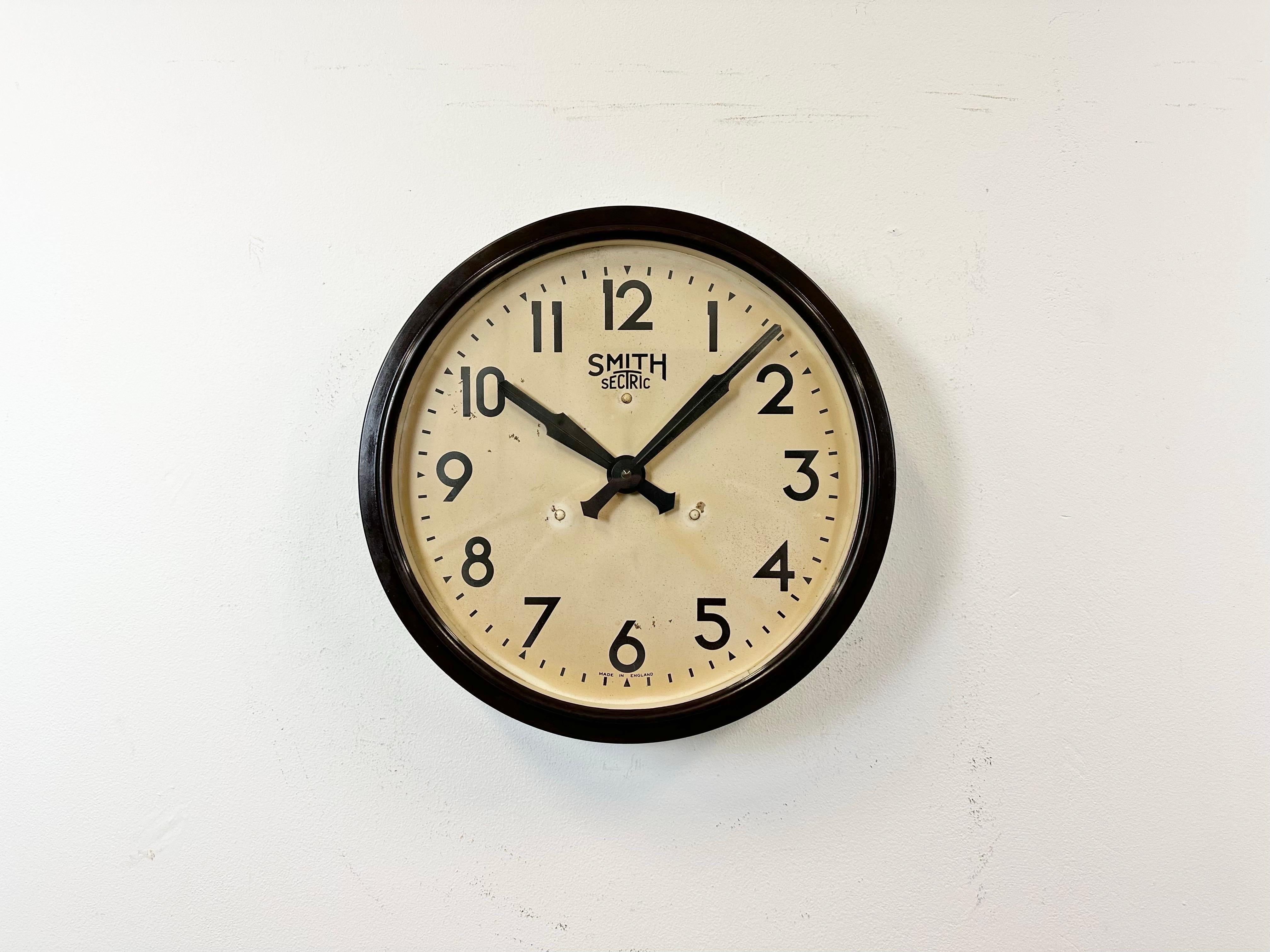 This wall clock was produced by Smith Sectric in England during the 1950s. It features a brown bakelite frame, an iron dial, an aluminium hands and a clear glass cover. The piece has been converted into a battery-powered clockwork and requires only