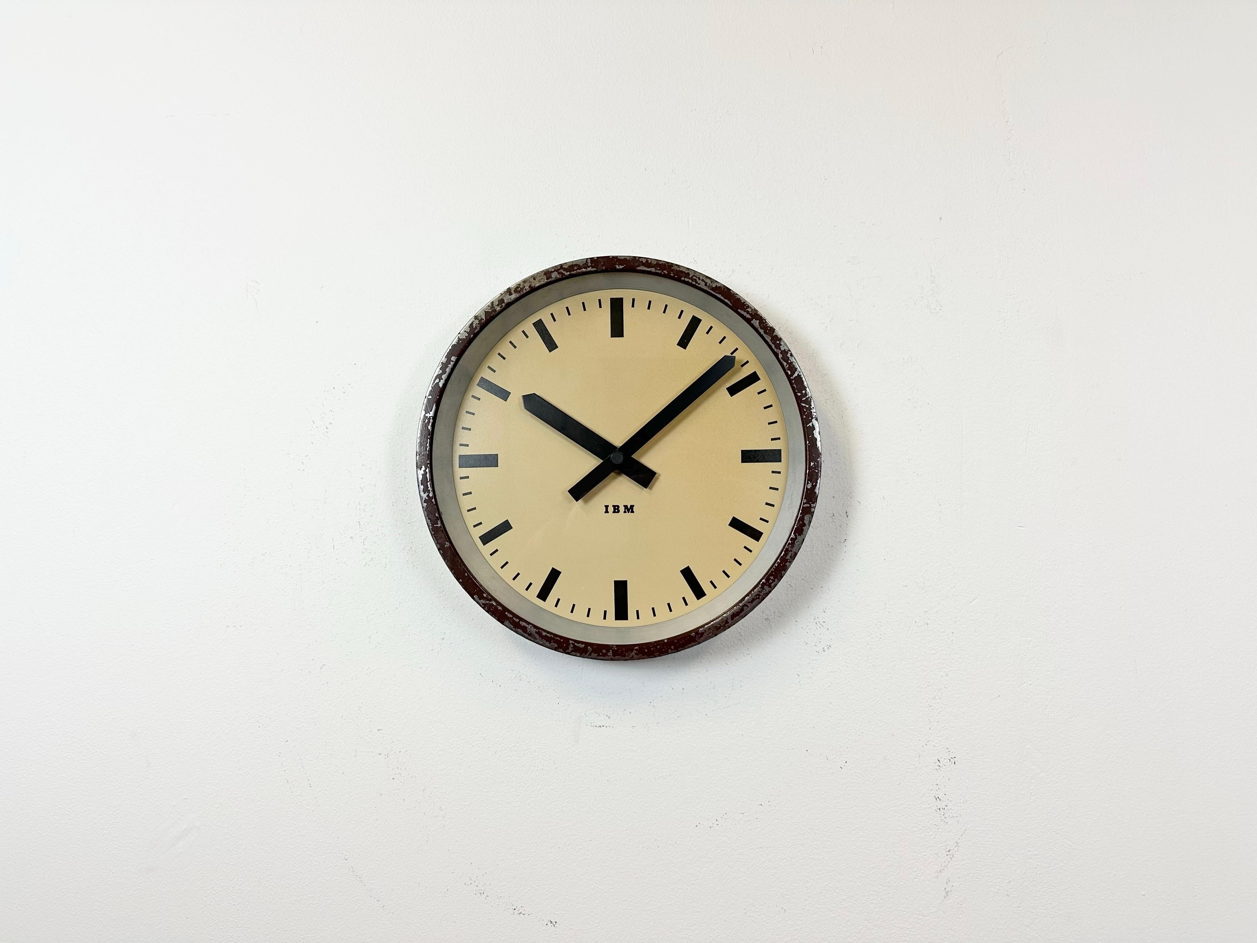 This wall clock was produced by IBM in USA during the 1950s. It features a brown metal frame, iron dial, aluminium hands and a clear glass cover. The piece has been converted into a battery-powered clockwork and requires only one AA-battery. The