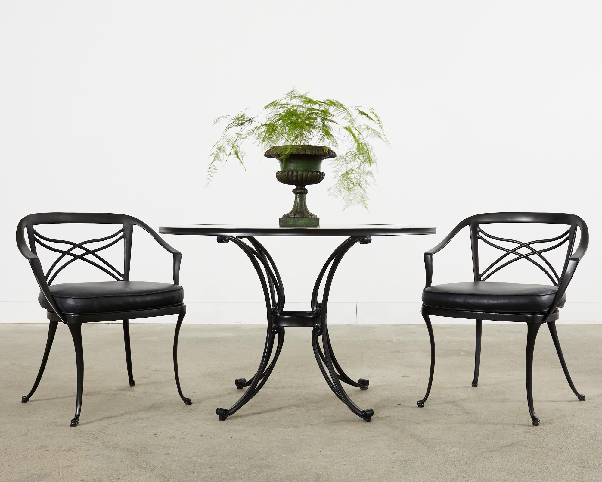 Neoclassical style patio and garden suite consisting of a glass top dining table and four dining chairs. Known as the classic collection by Brown Jordan. Constructed from gracefully curved cast aluminum with a later black paint finish. The round