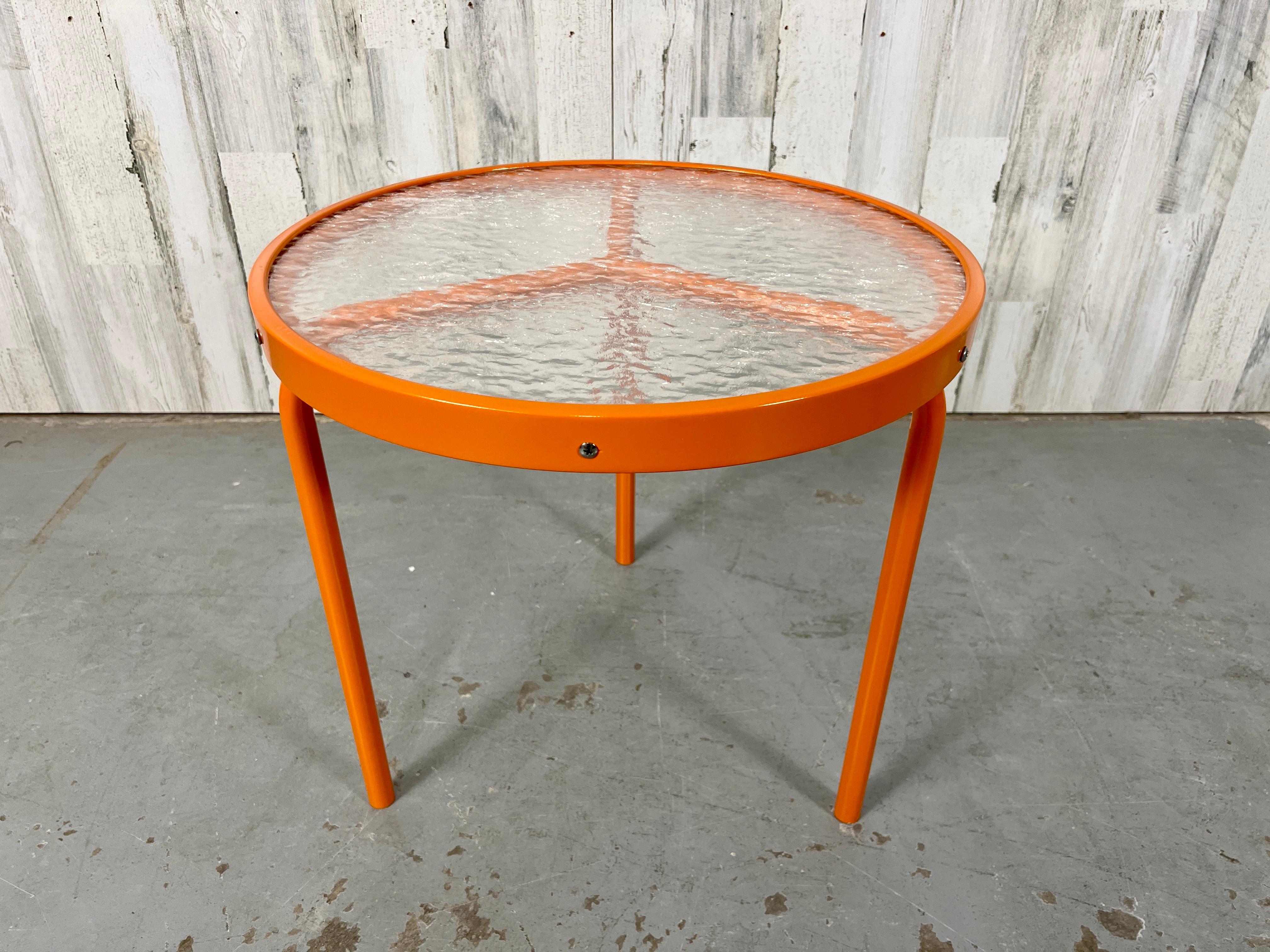 Round three legged side table newly powder coated in citrus orange. This table has the Peace symbol design where the three legs come together. Original pebble acrylic top does show some wear.