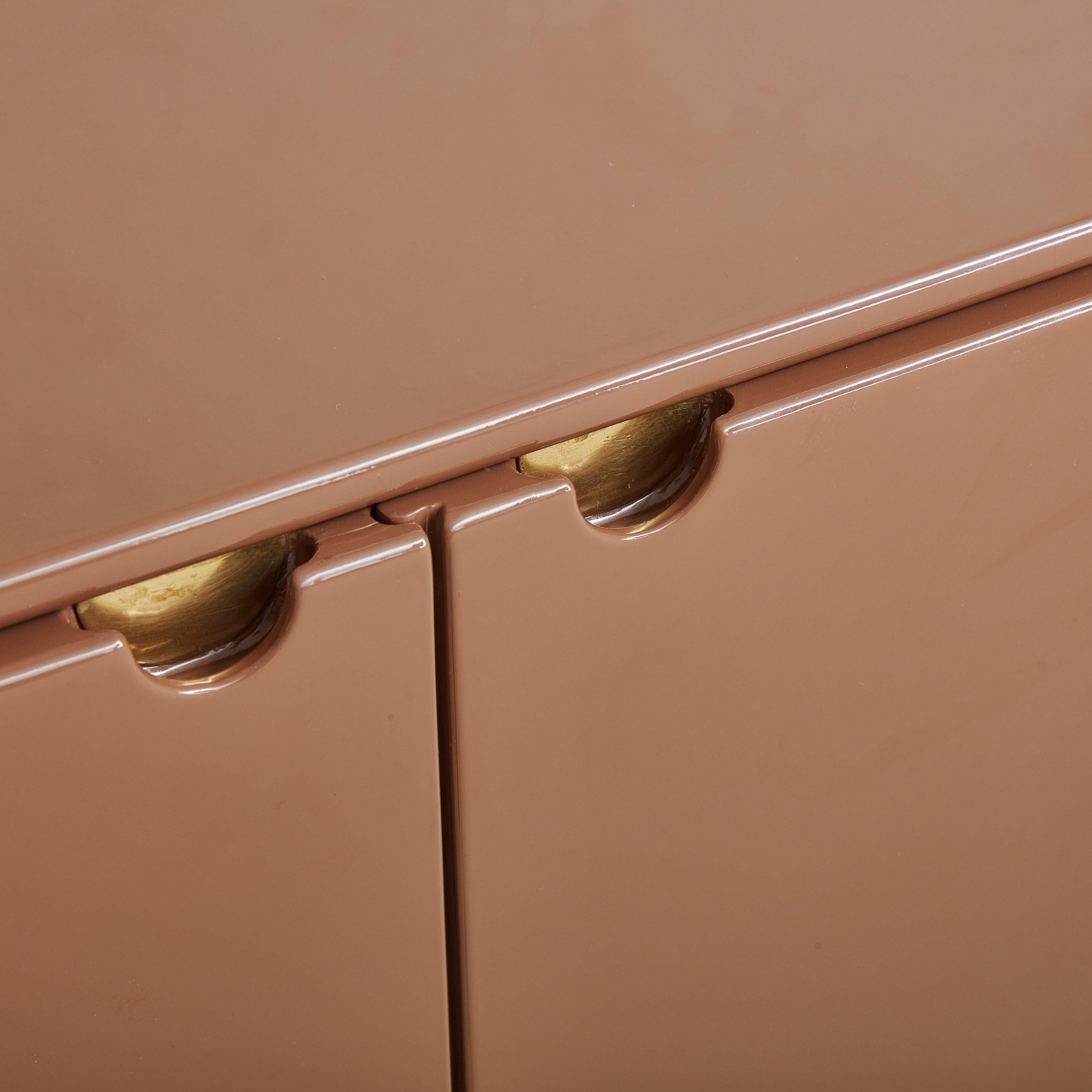 A 1970s Italian demilune credenza attributed to Mario Sabot. This gorgeous credenza features a rounded silhouette composed of lacquered wood in a rich, chocolate hue. The frame is supported by a contrasting brass base. Two flat paneled doors with
