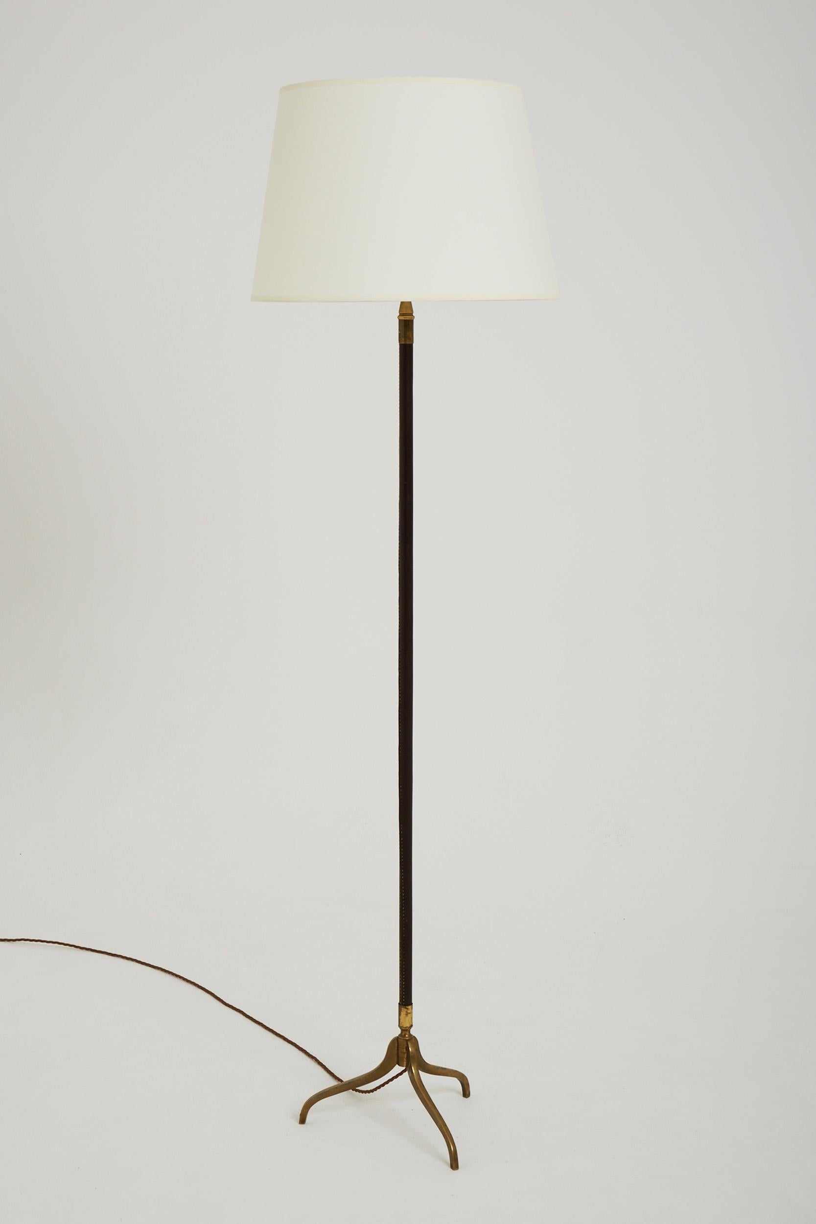 A saddle-stitched dark brown leather and brass tripod floor lamp.
France, Circa 1950.