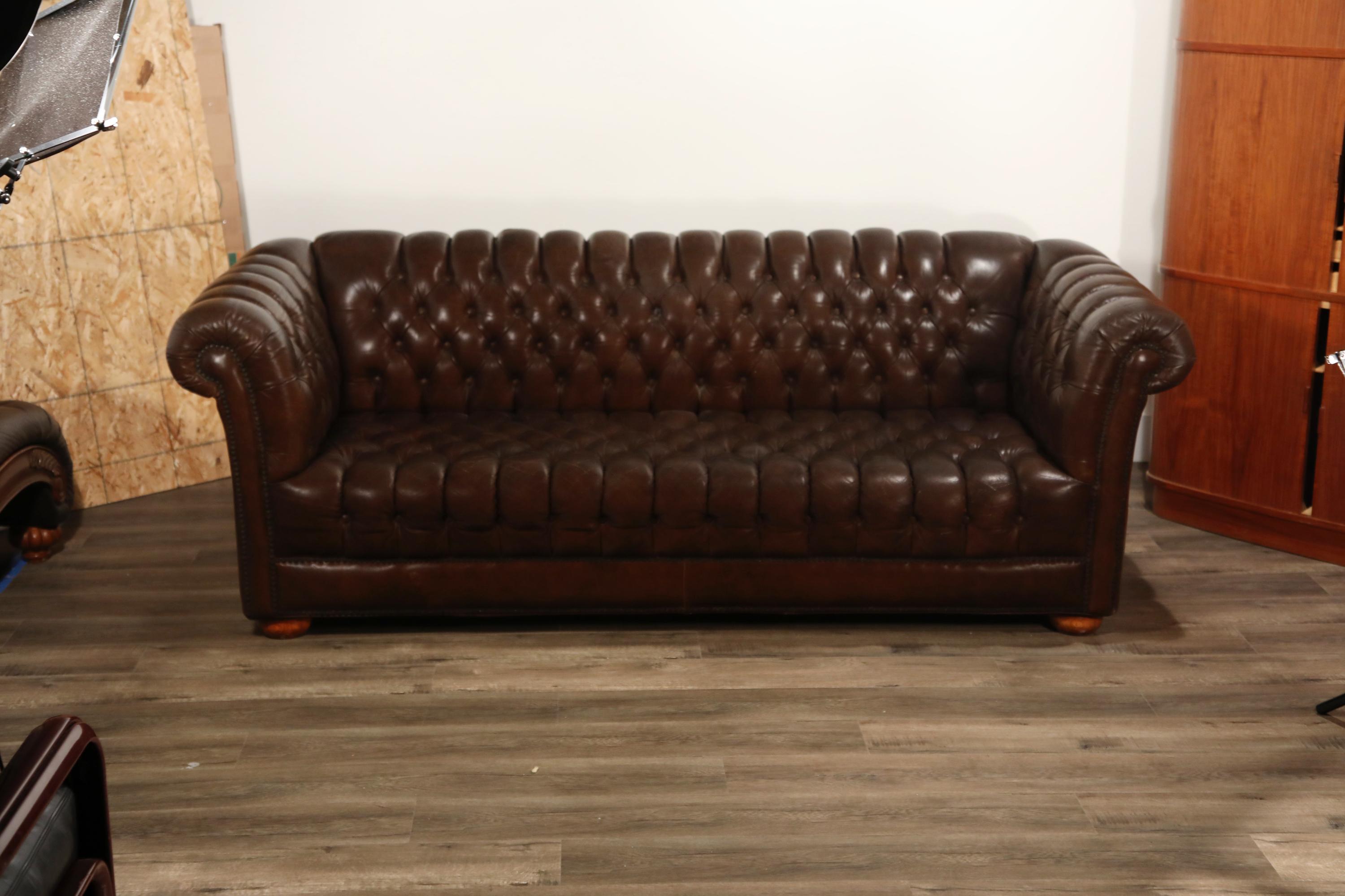 Handsome brown leather Chesterfield sofa displaying the classic attributes of this time honored design including the rolled back and armrests. This sofa is upholstered in a rich brown leather which has developed an admirable patina. The seat, inside