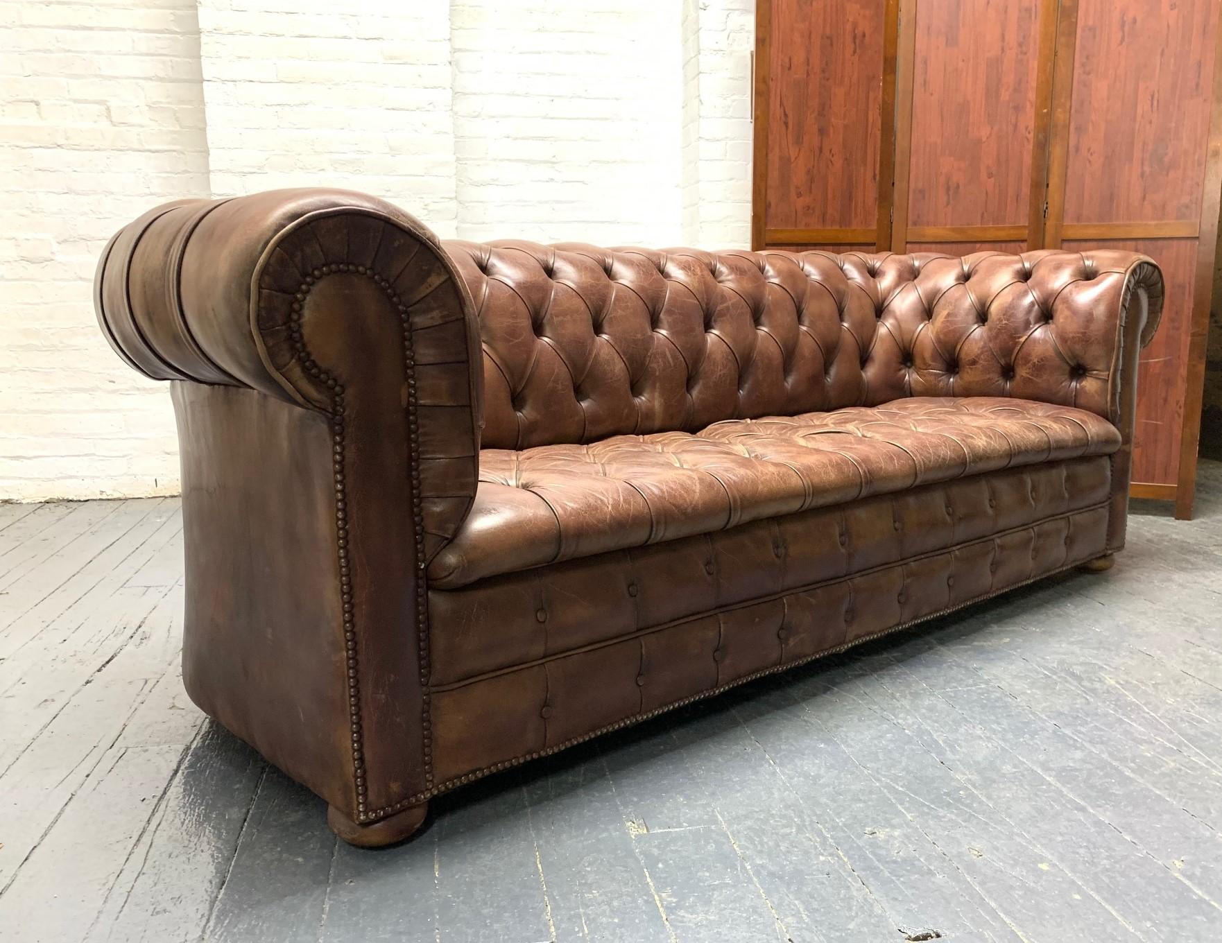 Chesterfield sofa in brown tufted leather, round wood bun feet, and brass nailhead trim.