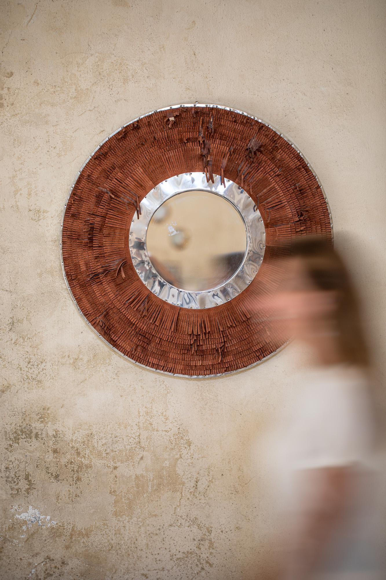 Unique round mirror, with a frame made of leather fringe. The mirror is composed by a central round mirror, surrounded by a crome circle frame and an external circle frame made of brown leather fringe.
  