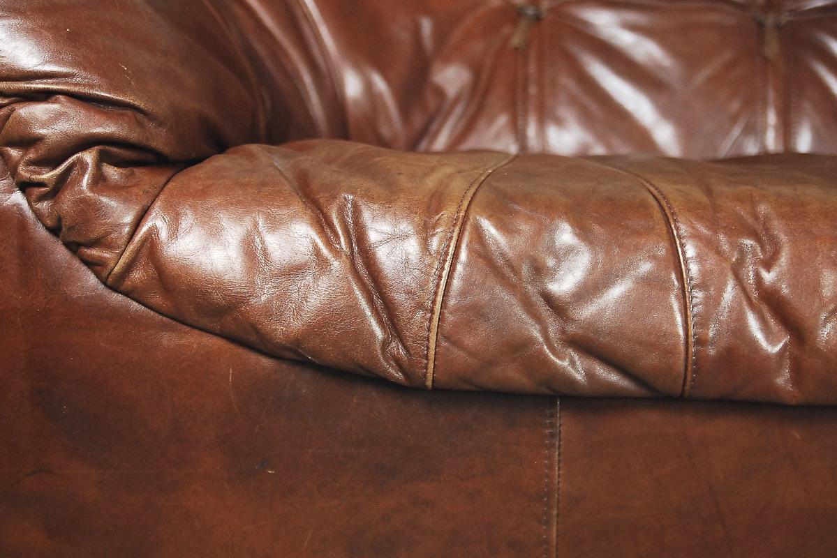 This charming loveseat was manufactured in Netherlands during the 1970s. The round-shaped sofa was upholstered in many pieces of brown genuine leather. The leather has a natural beautiful patina and can be remove, because it has a hide zip on the