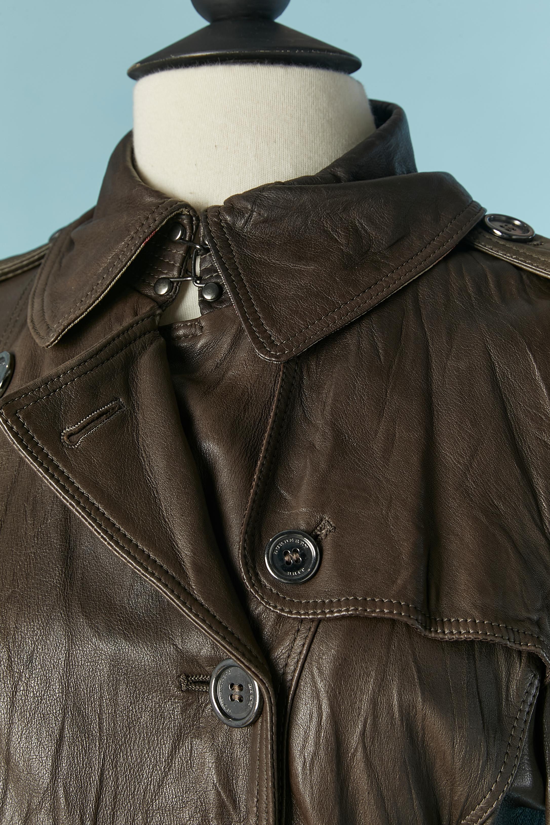 Trench in pelle marrone. fodera in cotone all'interno delle spalle e sul davanti e fodera in rayon nella parte inferiore del cappotto e all'interno delle maniche. 
Chiusura con bottone e asola con marchio sul davanti. Cintura in pelle e fibbia in