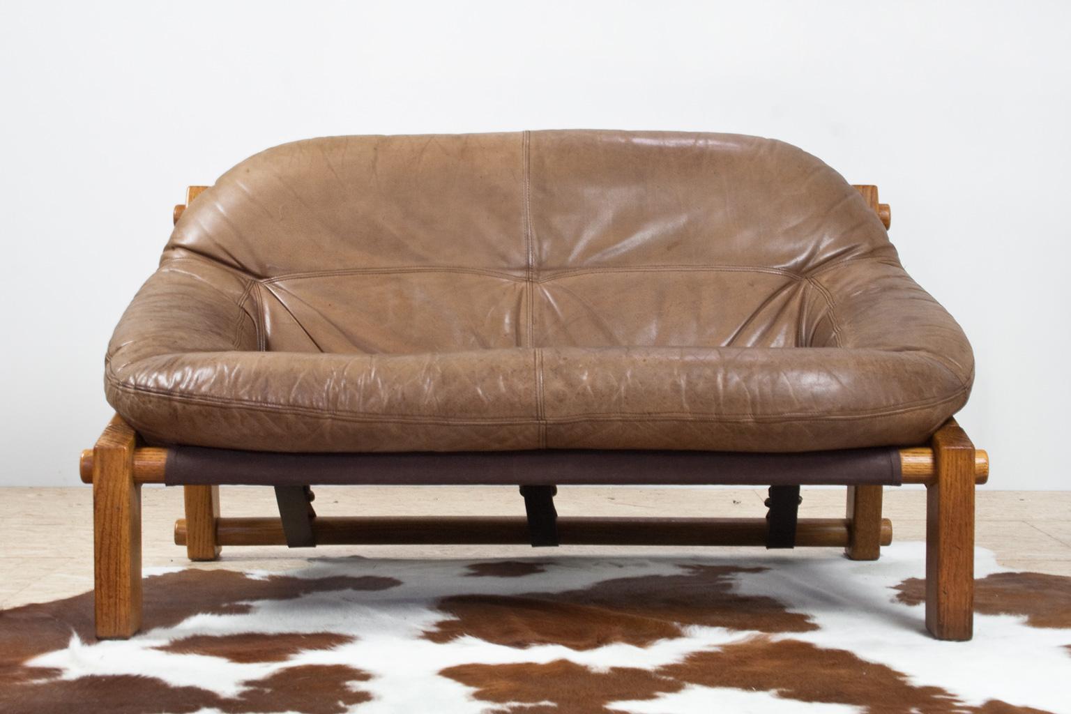 Two-seat Brutalist sofa in soft toned brown leather designed by Dutch designer Gerard Van Den Berg in the 1970s. This two person sofa is brutally oversized with a clear view of the solid pine wooden construction. The leather straps in the back are