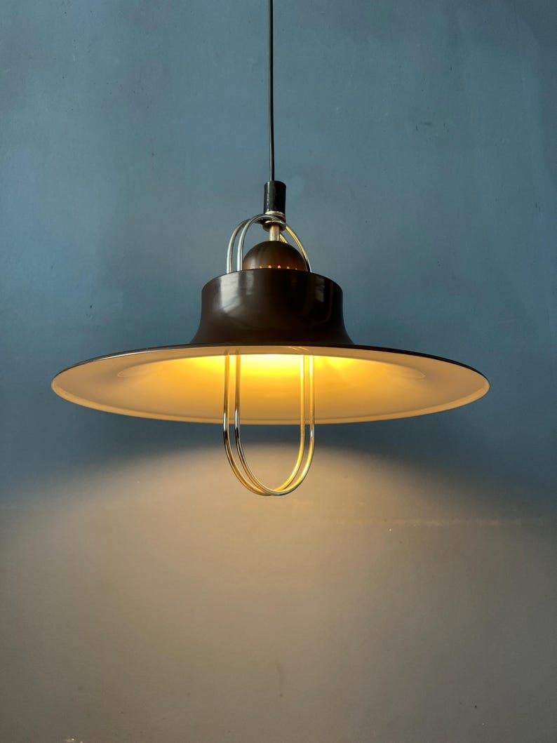 Brown mid century UFO pendant lamp with chrome details. The lamp is made out of metal and has a flying saucer-like shape. The lamp requires one E27/26 lightbulb.

Additional information:
Materials: Metal
Period: 1970s
Dimensions: Width: 31