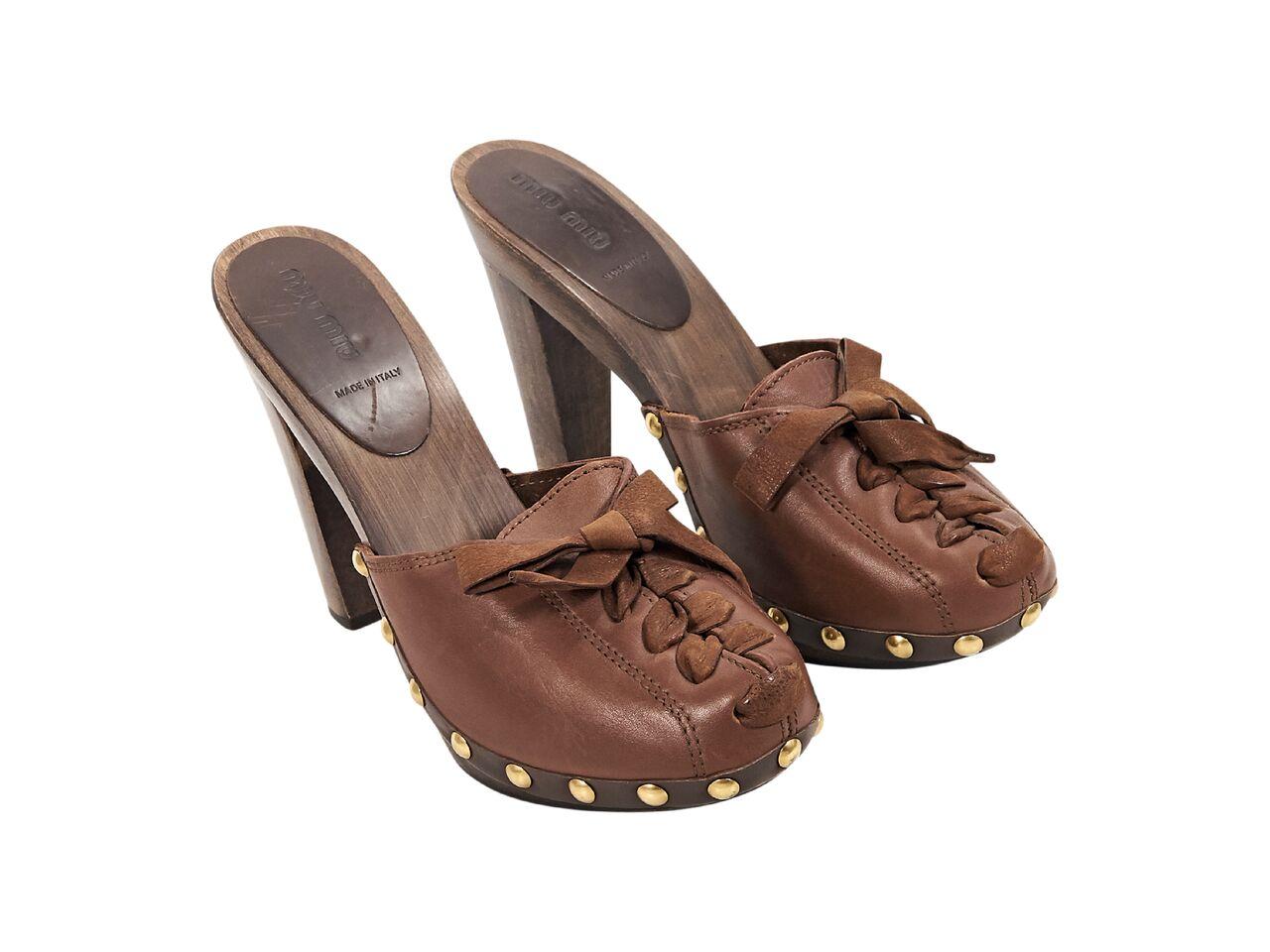 Product details:  Brown leather heeled mules by Miu Miu.  Accented with studs.  Lace-up front panel.  Round toe.  Wooden heel and platform.  Slip-on style.  Goldtone hardware.  5