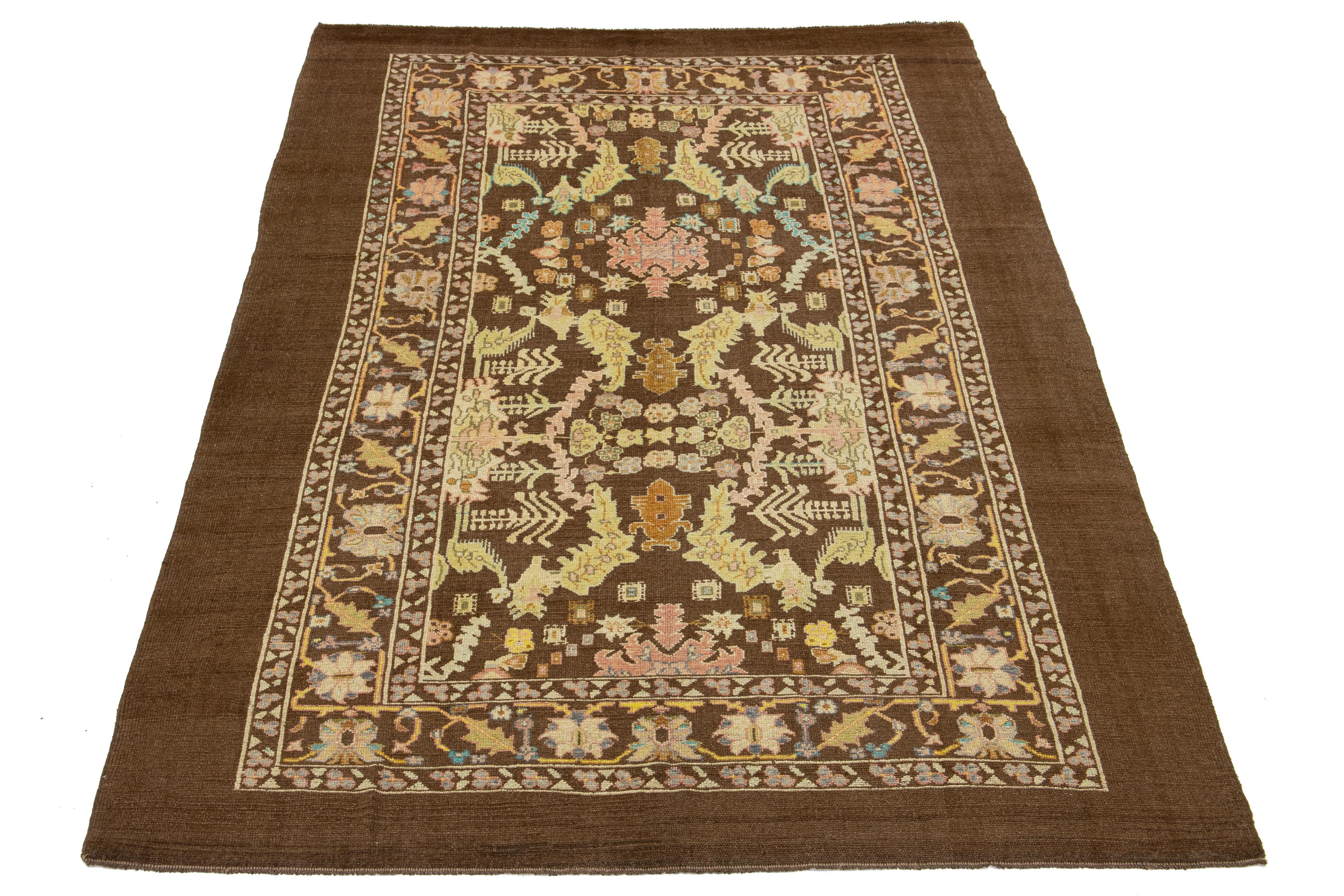 This modern hand-knotted wool rug from the Apadana Revival Collection features a brown background and a striking botanical floral design with multicolored shades. 

This rug measures 8'2