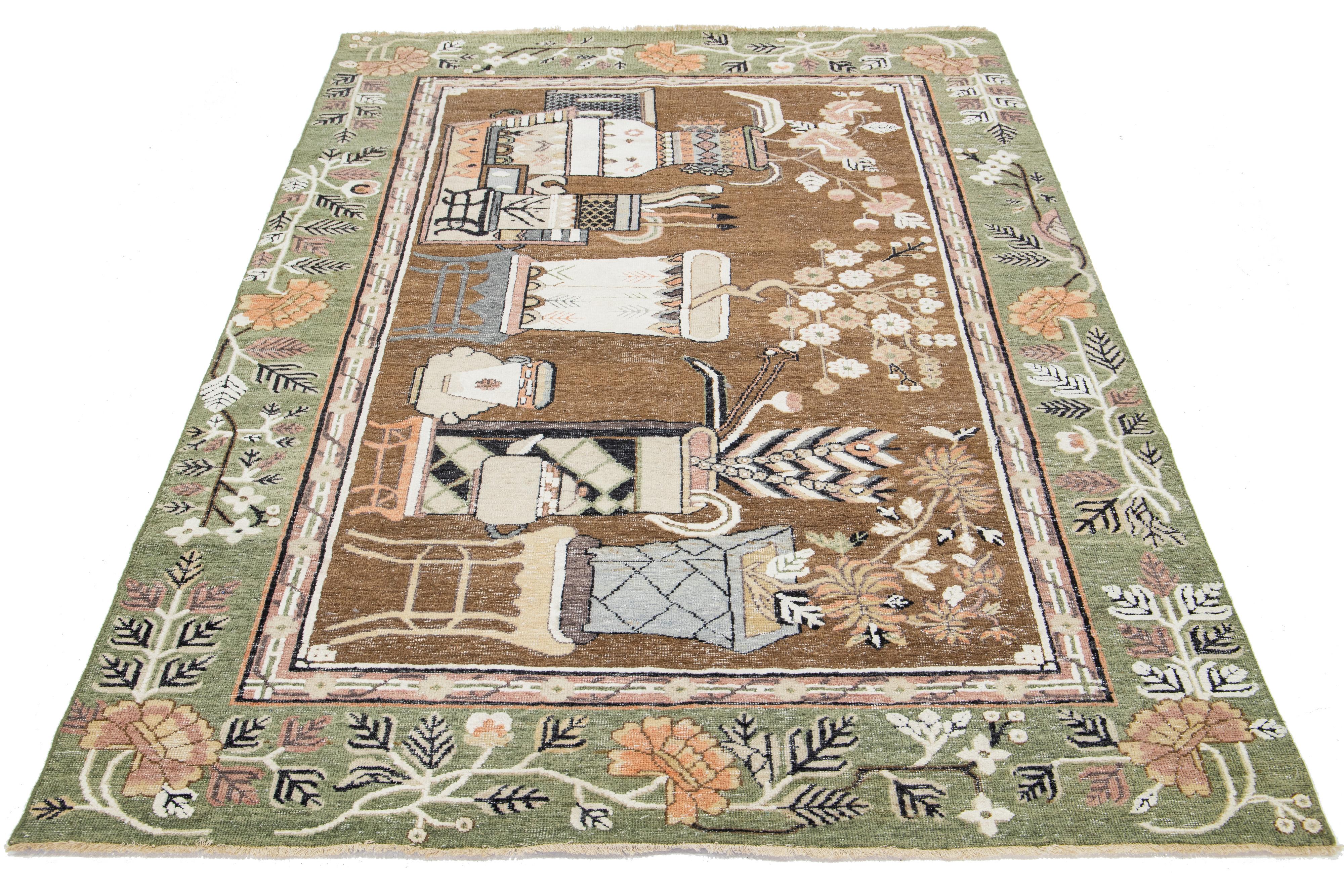 Dieser schöne moderne Samarkand-Teppich aus handgeknüpfter Wolle hat ein braunes Feld und einen grünen Rahmen. Der Teppich zeigt orange, graue und rosafarbene Akzente in einem malerischen Design.

Dieser Teppich misst 6'1