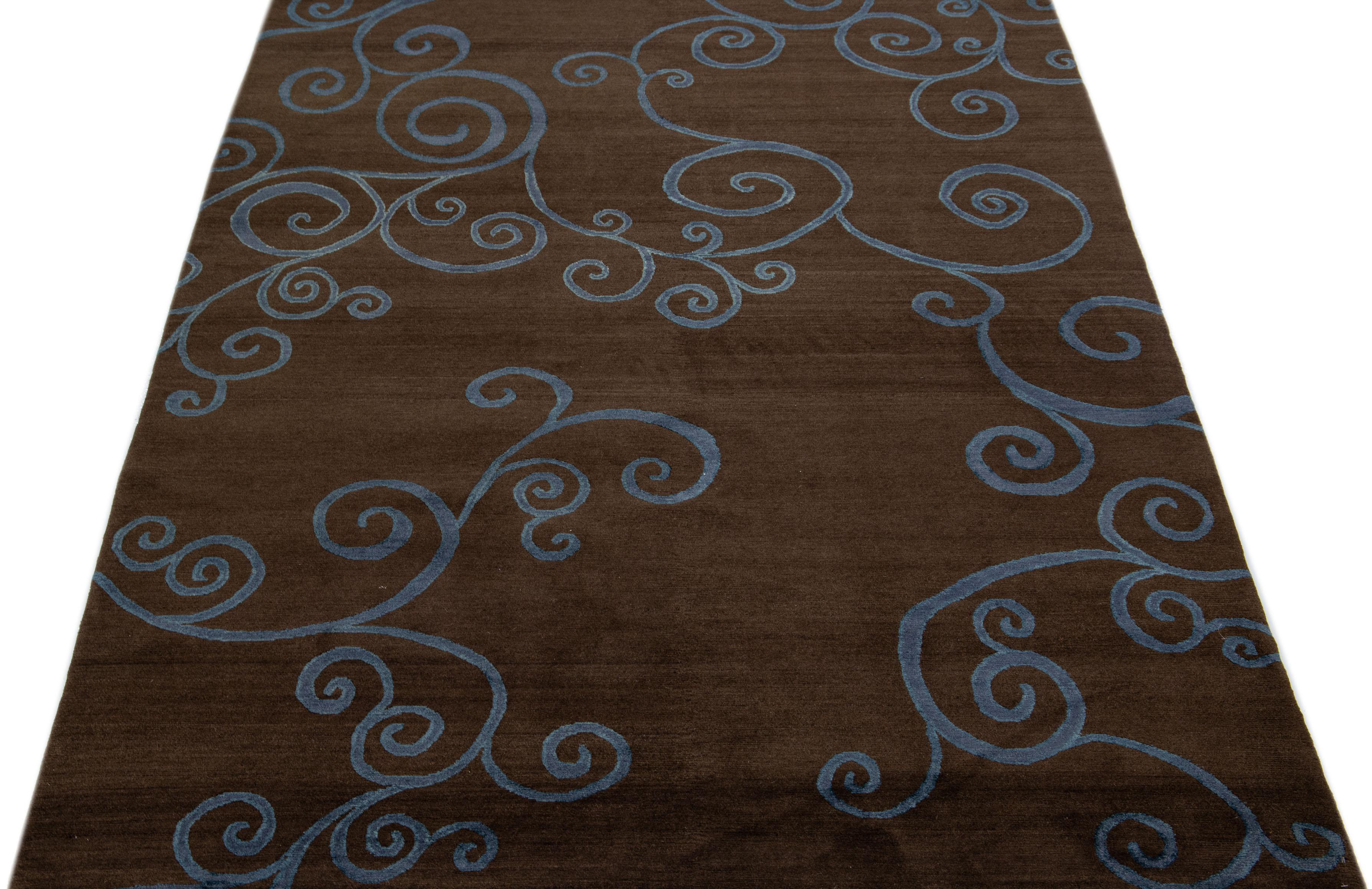 Ce tapis tibétain contemporain est confectionné à la main avec de la laine et de la soie et présente un champ de couleurs marron saisissant. Un motif géométrique abstrait en bleu sur tout le pourtour ajoute à son charme.

Ce tapis mesure 6' x 9'.