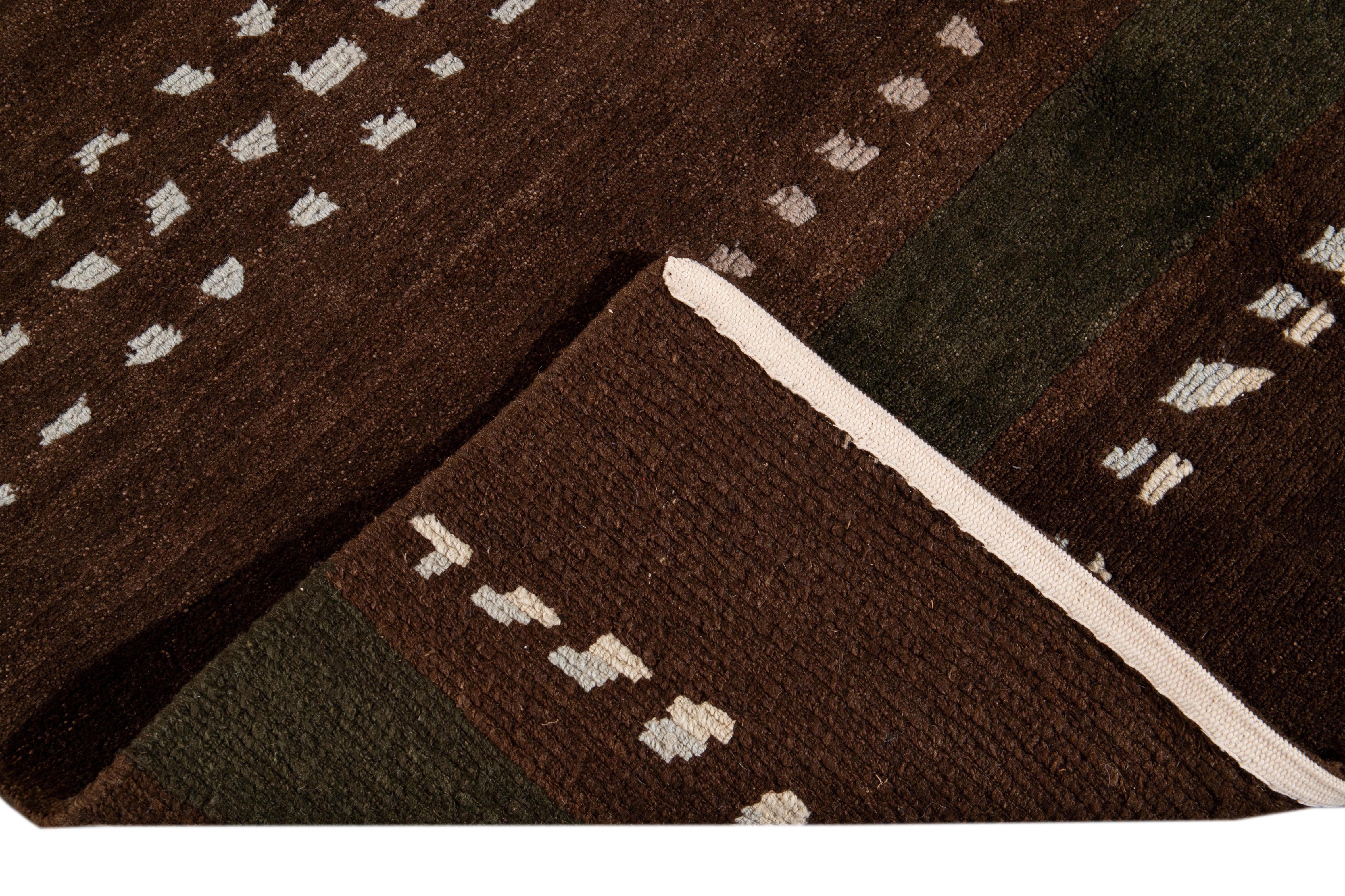 Schöner moderner tibetischer handgeknüpfter Wollteppich mit braunem Feld. Dieser tibetische Teppich hat elfenbeinfarbene, beigefarbene und grüne Akzente in einem prächtigen geometrischen Streifendesign.

Dieser Teppich Measures: 8' x 10'.