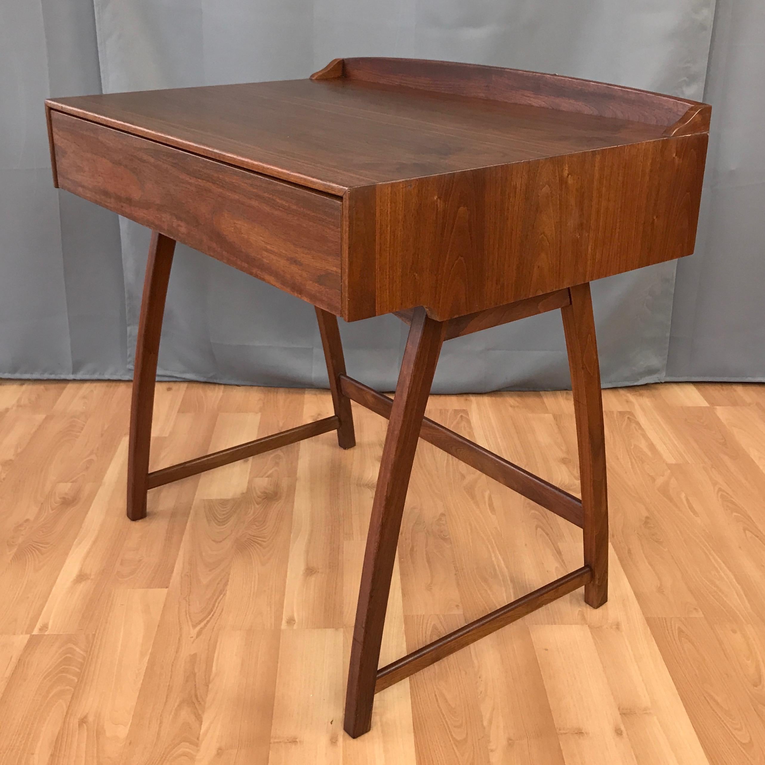 An uncommon early 1960s Brown-Saltman small walnut desk with drawer.

Top displays handsome bookmatched grain, while arced legs and backstop provide a perfect amount of personality. Drawer features built-in organizer and retains original