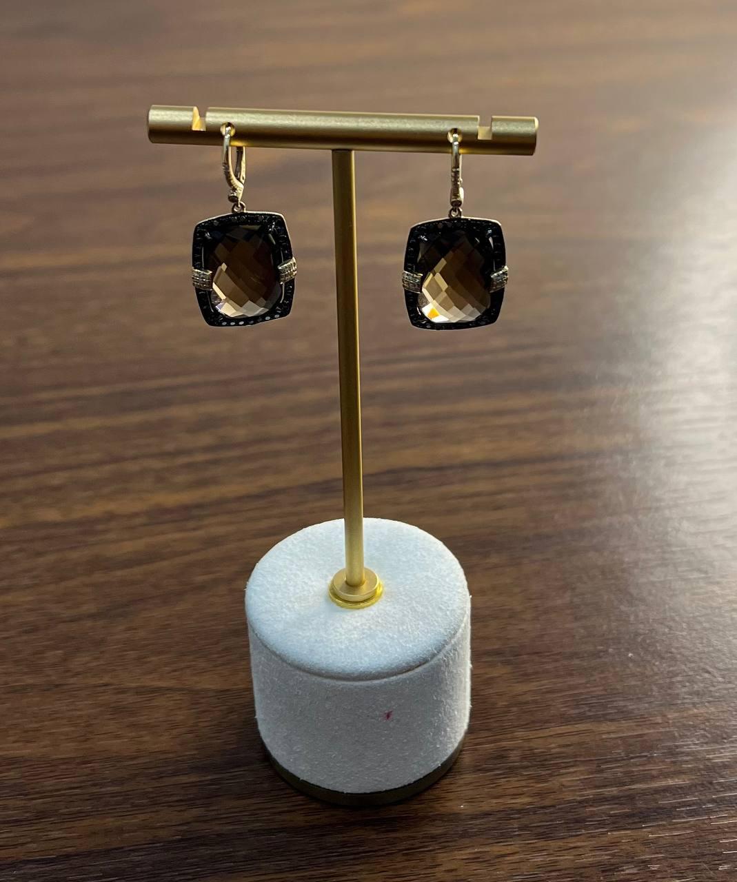 Un paio di orecchini di grande effetto ed eleganza. Questi orecchini presentano pietre sfaccettate di forma quadrata con una ricca tonalità fumé.
Ogni pietra è incorniciata da un bordo scuro e strutturato e arricchita da una fascia di dettagli