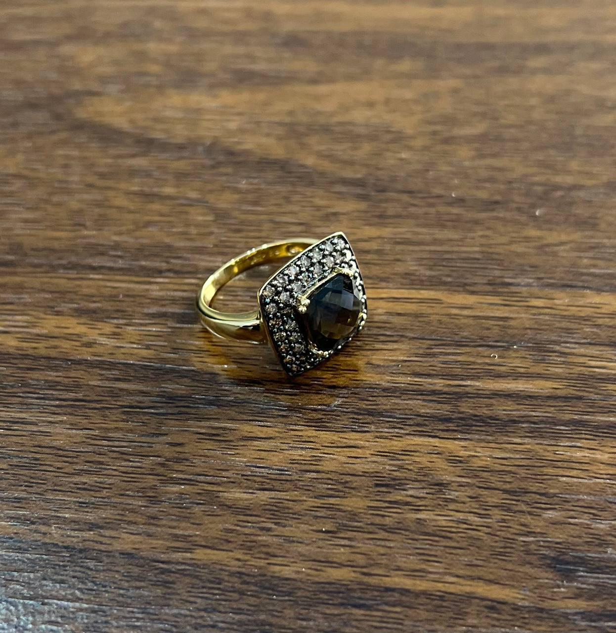This elegant ring by Galt & Bro. Jewelers is crafted in gold. It features a striking dark gemstone at its center, surrounded by a halo of sparkling smaller stones.
The setting is square-shaped, enhancing the central stone's allure.
2.65 CT Smoky