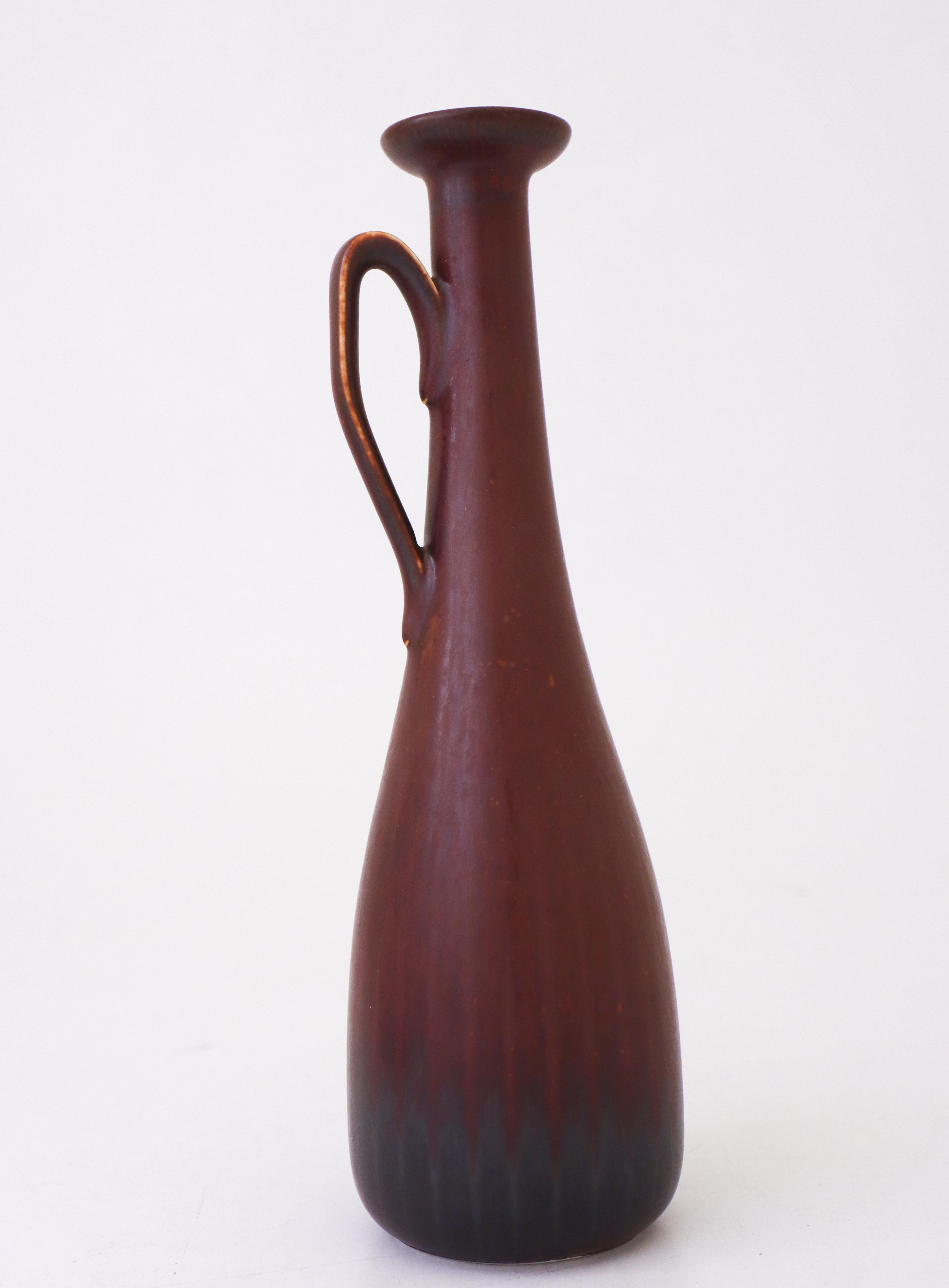 Die braune Vase wurde von Gunnar Nylund in Rörstrand entworfen. Sie ist 25 cm hoch und hat einen Durchmesser von 7 cm (2,8