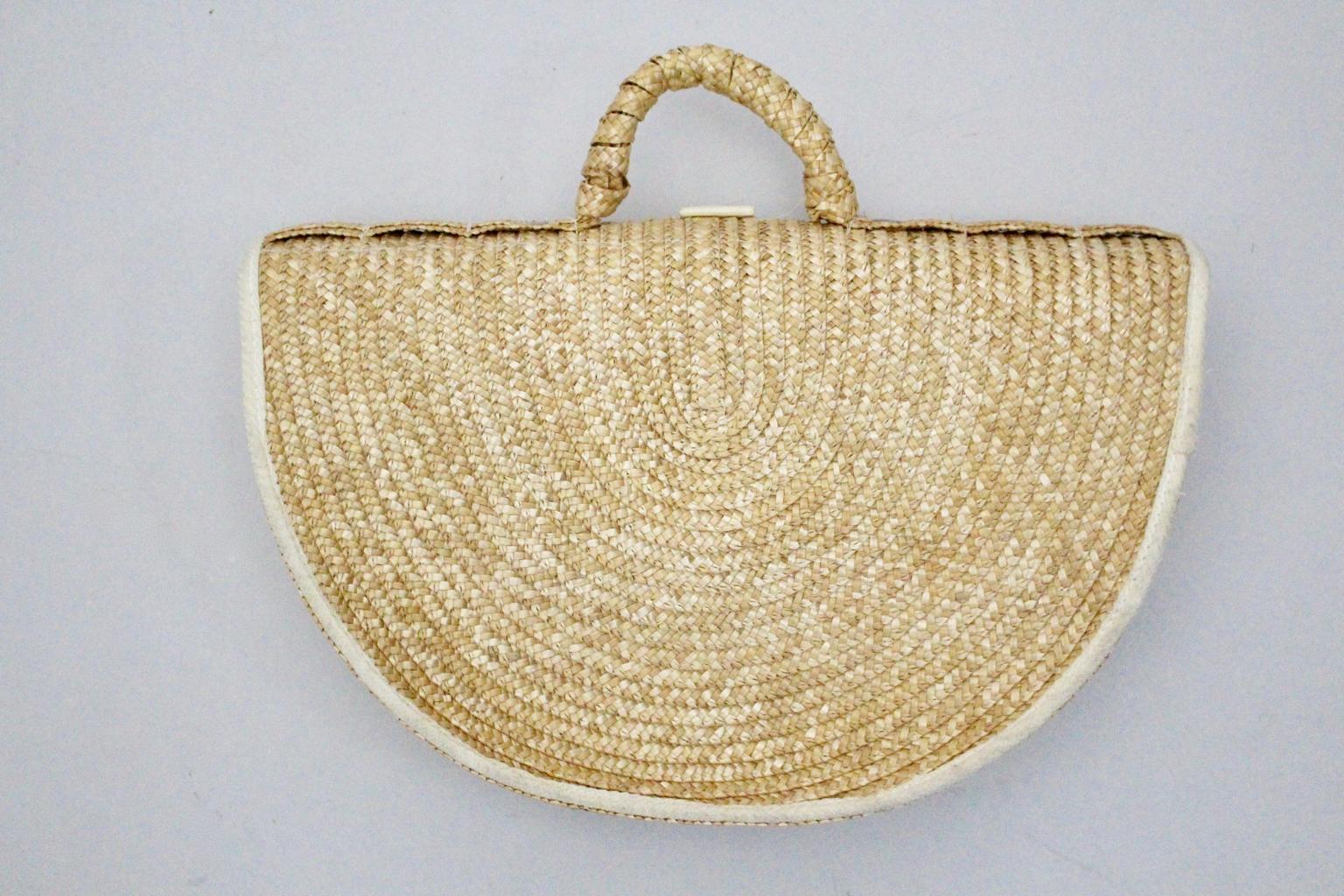 The handle bag was made of straw and shows a decoration with wooden rings and canvas in an extraordinary halfround shape.
Furthermore the handle bag shows a snap button closure. The lining was made of white canvas and features also a small side
