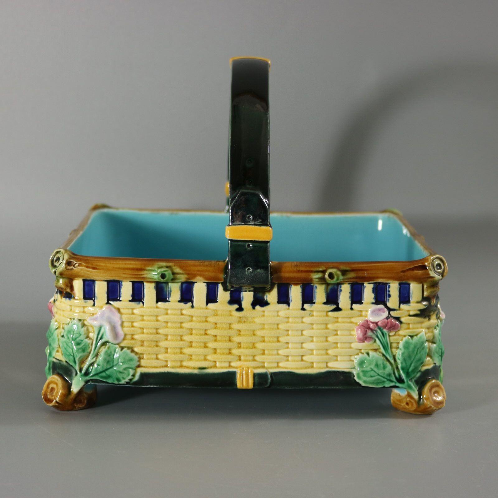 Cestino in maiolica Brown Westhead & Co. con fiori ai quattro angoli, lati in stile intreccio di cesti e manico modellato a forma di cinturino in pelle con fibbie. Colorazione: predominano il giallo, il verde e il blu cobalto. Porta un numero di