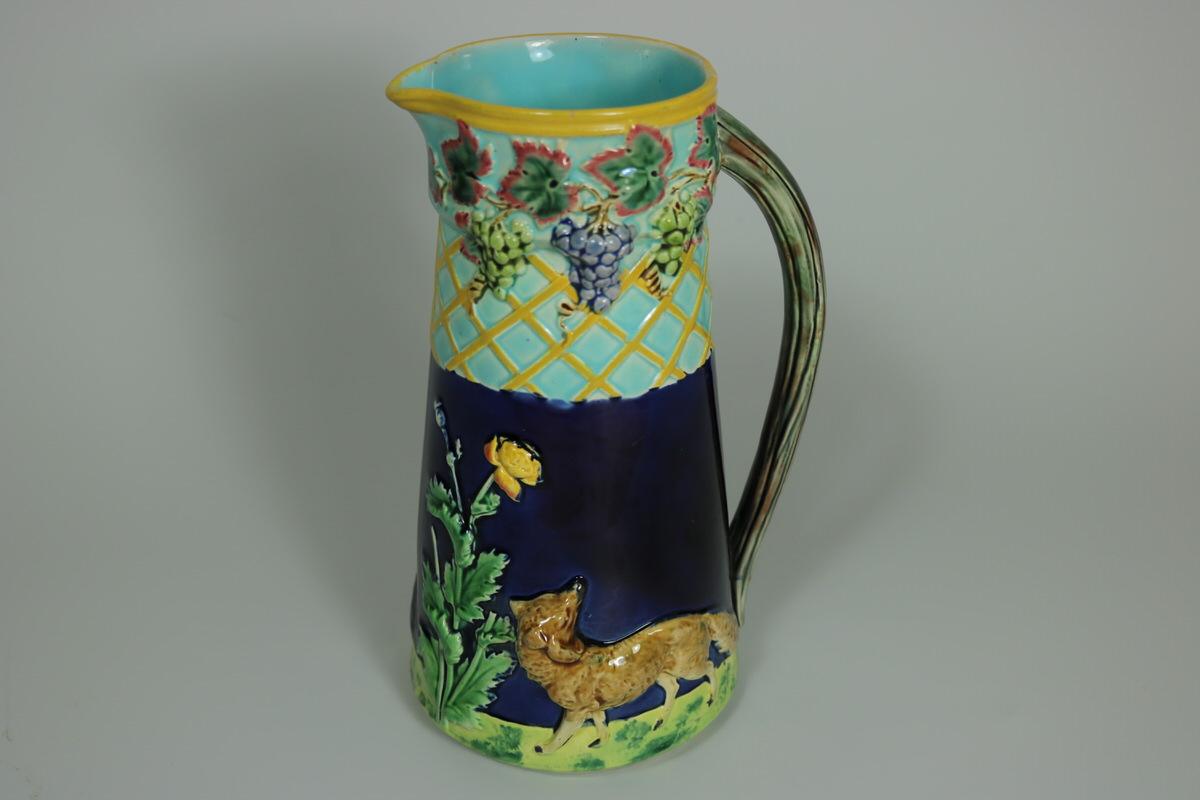 Brown Westhead Moore and Co Majolica jug/pitcher which features a fox on either side at the bottom, with a grapevine border to the top. Coloration: Cobalt blue, turquoise, ochre, are predominant. Bears a pattern number, '341'. English diamond