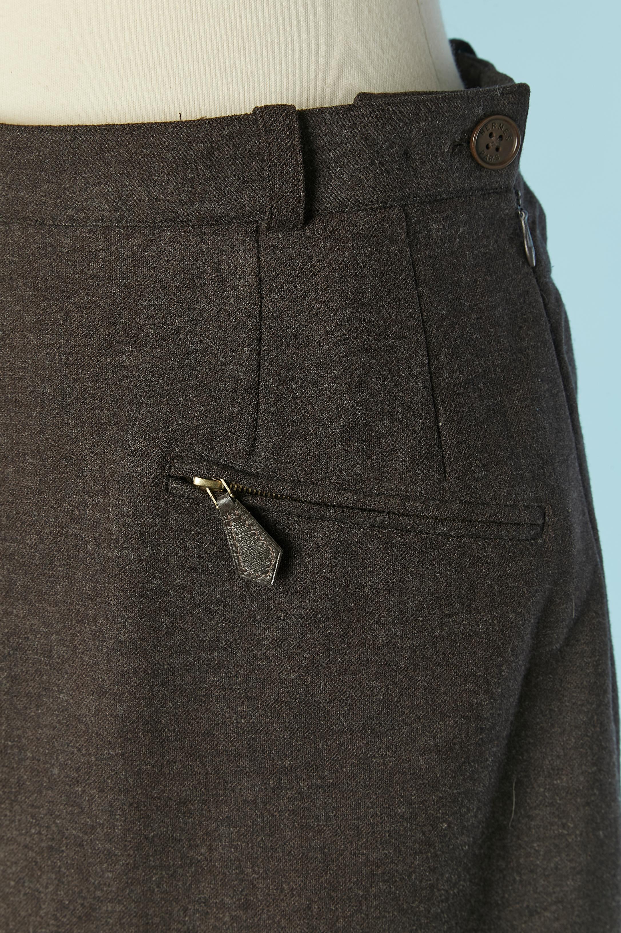 Brown wool skirt . Main fabric composition: 92% wool, 5% nylon, 3% lycra. Lining composition: 60% acetate, 40% bemberg. 
Pocket on the front with zip closure and leather zip-puller. Branded button, buttonhole and zip closure on the left side.
No