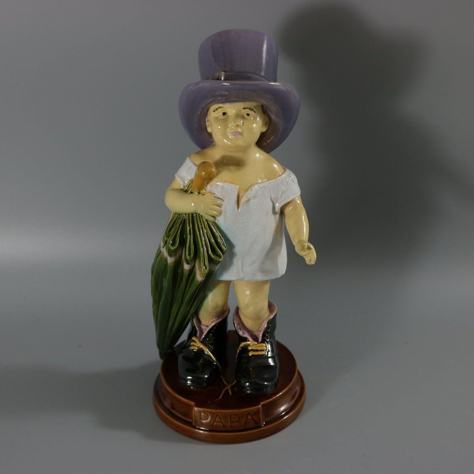 Brownfield Majolica figure which features a young child wearing a grown ups hat and shoes, carrying an umbrella. Title, 'PAPA' molded into the base - French and Spanish for Dad. No doubt the child is wearing Dad's shoes and hat and carrying his