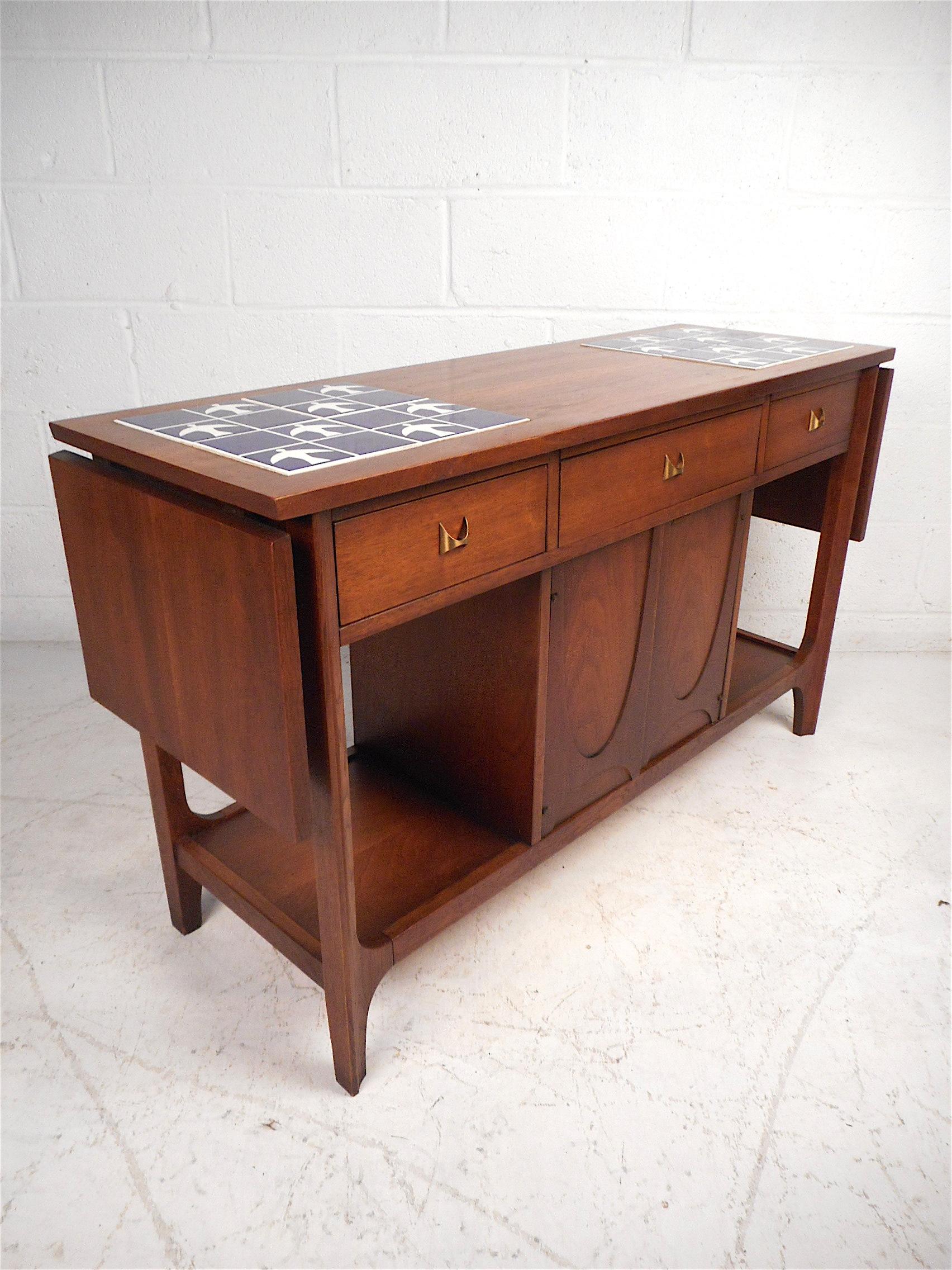 Beautiful Mid-Century Modern console table by Broyhill. Sturdy walnut construction with a finished back, two drop-leaf extensions on either side of the piece which extend the table's surface from 48 in. to 70.5 in. wide. Stylish design with sculpted