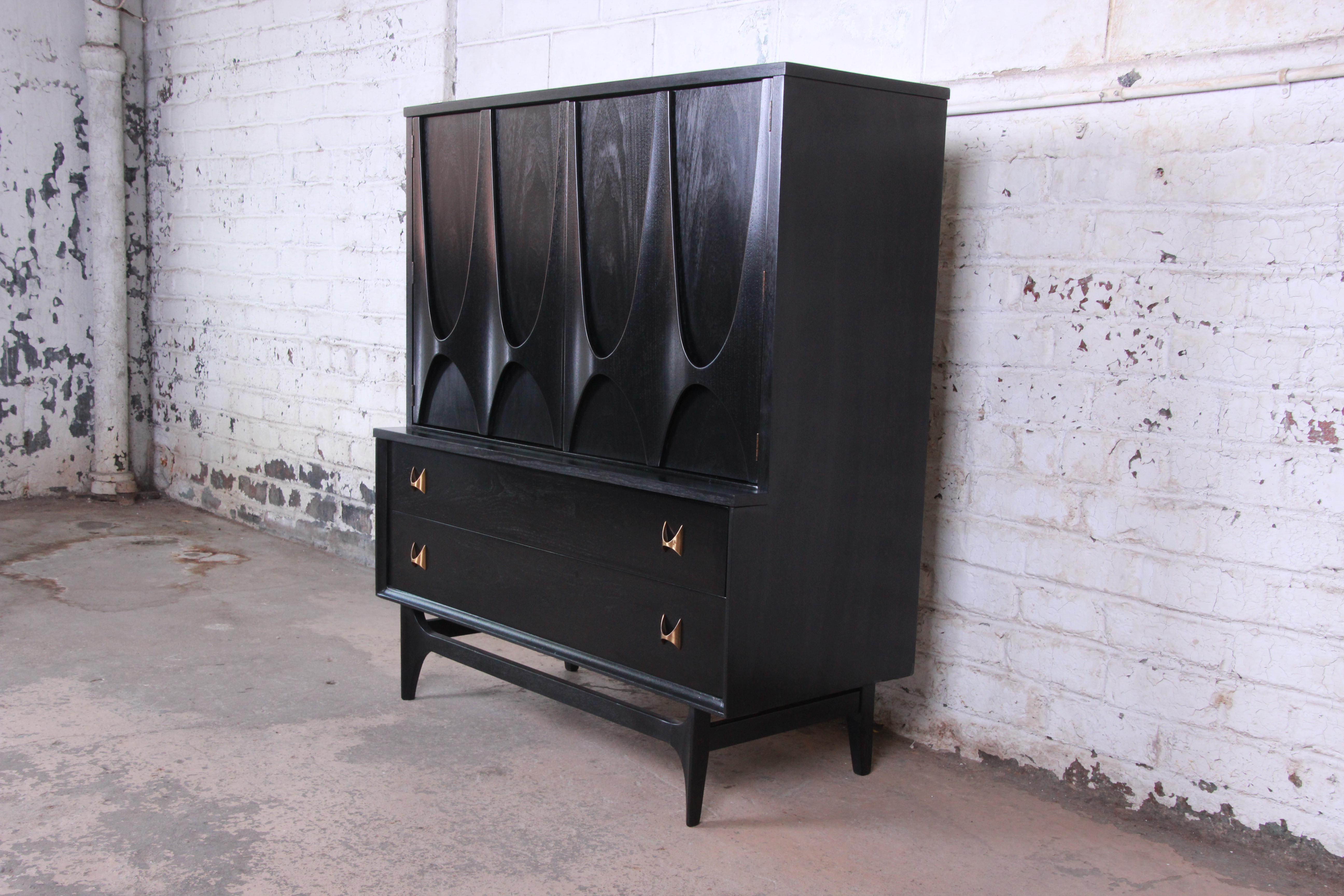 Offering a stunning Mid-Century Modern gentleman's chest or highboy dresser by Broyhill Brasilia. The chest features the iconic sculpted walnut design with newly ebonized finish and original sculpted arch brass pulls. It offers ample room for