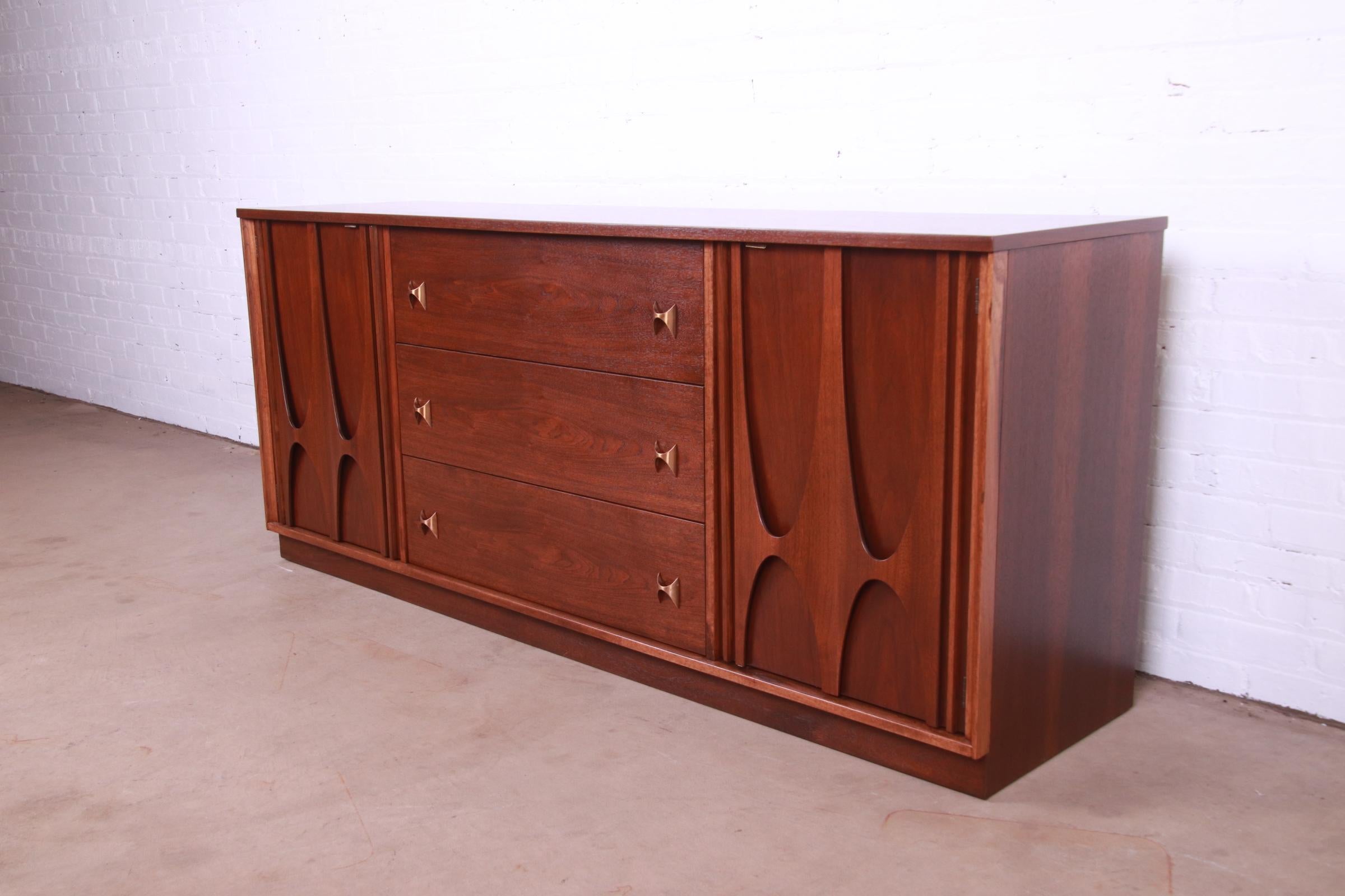 An exceptional Mid-Century Modern nine-drawer dresser or credenza

By Broyhill Brasilia

USA, 1960s

Sculpted walnut, with iconic brass arch drawer pulls.

Measures: 72