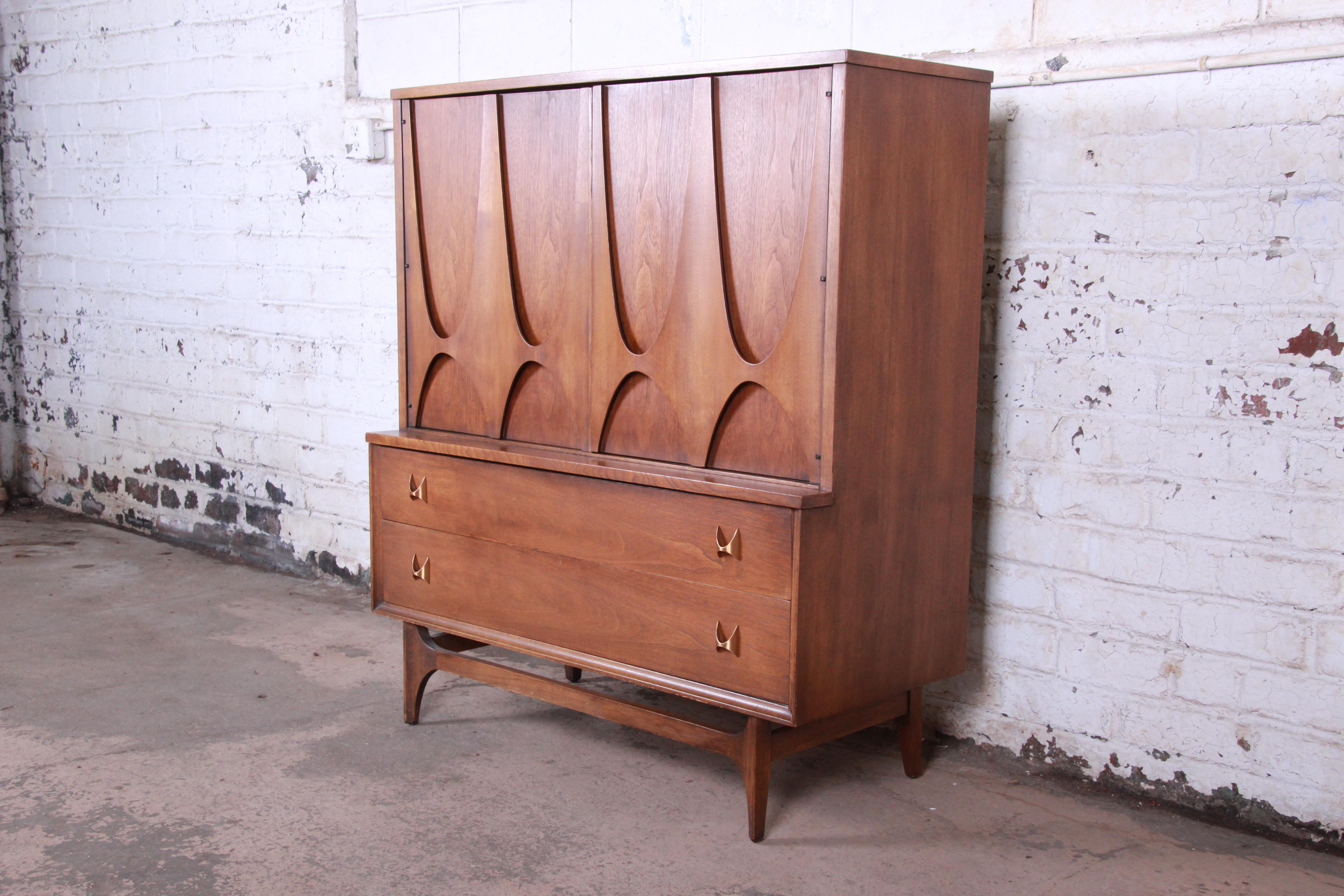 An exceptional and iconic Mid-Century Modern sculpted walnut gentleman's chest by Broyhill Brasilia. The chest has gorgeous walnut wood grain, sculpted arches, and original brass arch pulls. The two large cabinet doors open up to four dovetailed