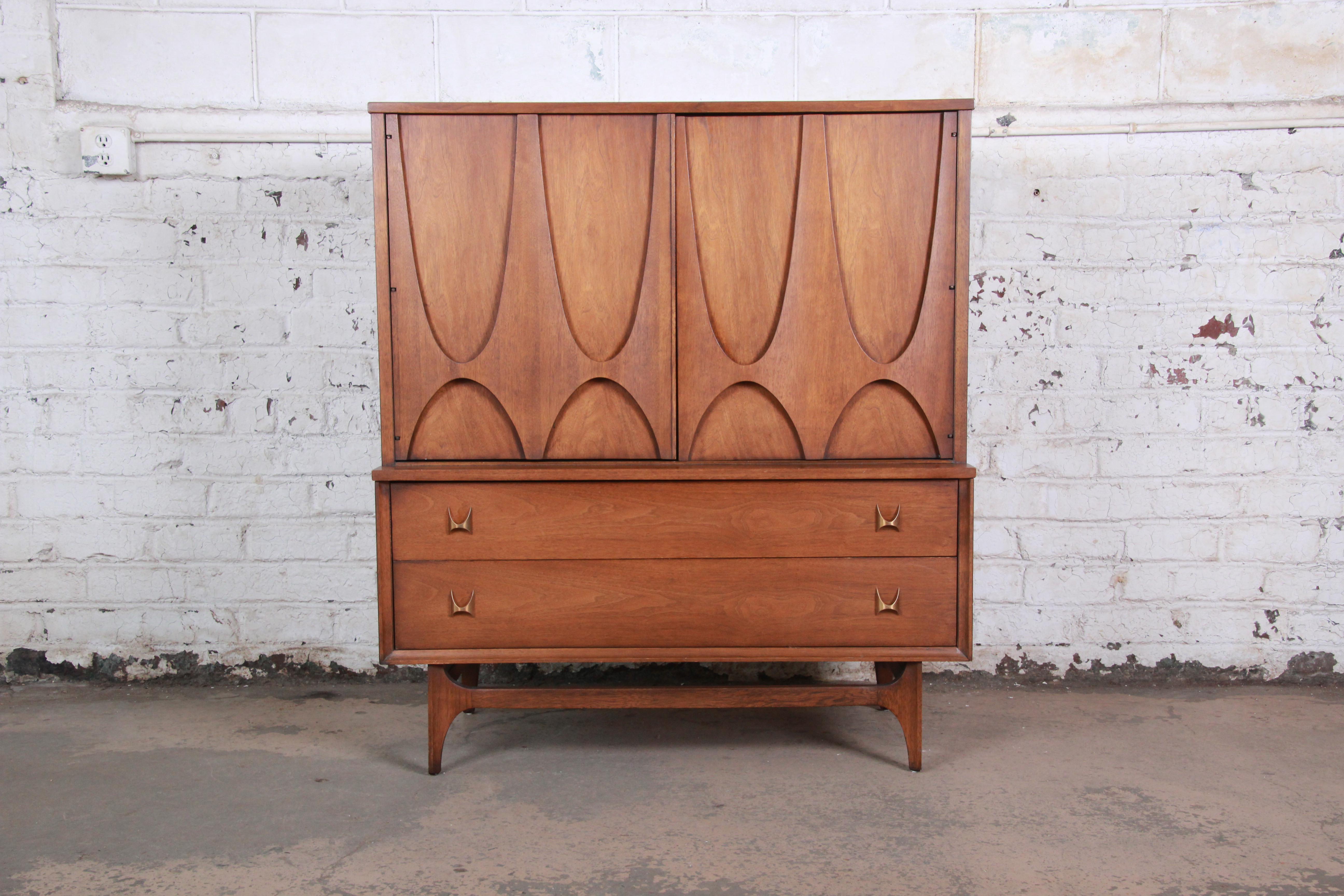 An exceptional and iconic Mid-Century Modern sculpted walnut gentleman's chest by Broyhill Brasilia. The chest has gorgeous walnut wood grain, sculpted arches and original brass arch pulls. The two large cabinet doors open up to four dovetailed